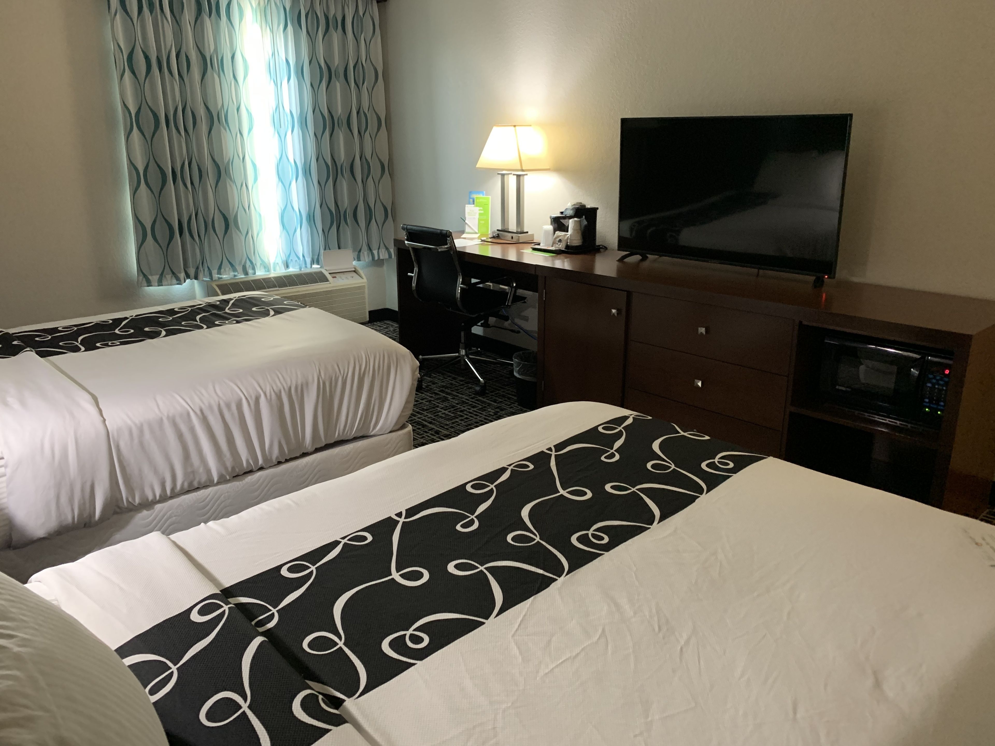 A hotel room with two beds, a desk, a TV, a lamp, and a microwave.