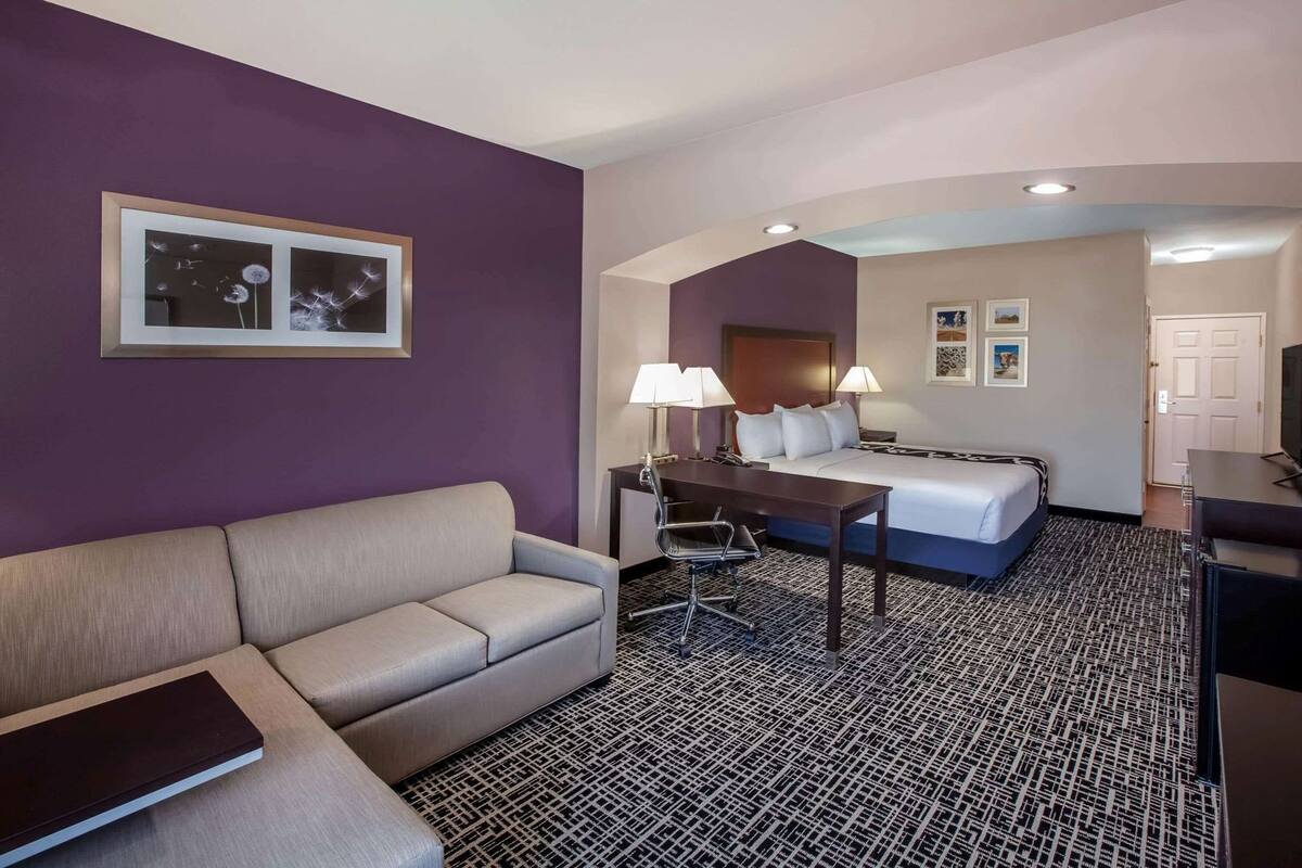 A hotel room with a sofa, a desk with a chair, a bed, and a TV.