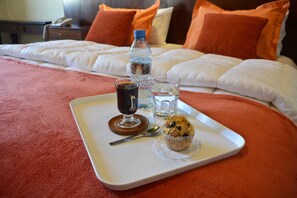 Un llit ben arreglat amb almoades taronges, una safata amb un muffin, un got d'aigua i una ampolla d'aigua en una habitació d'hotel.