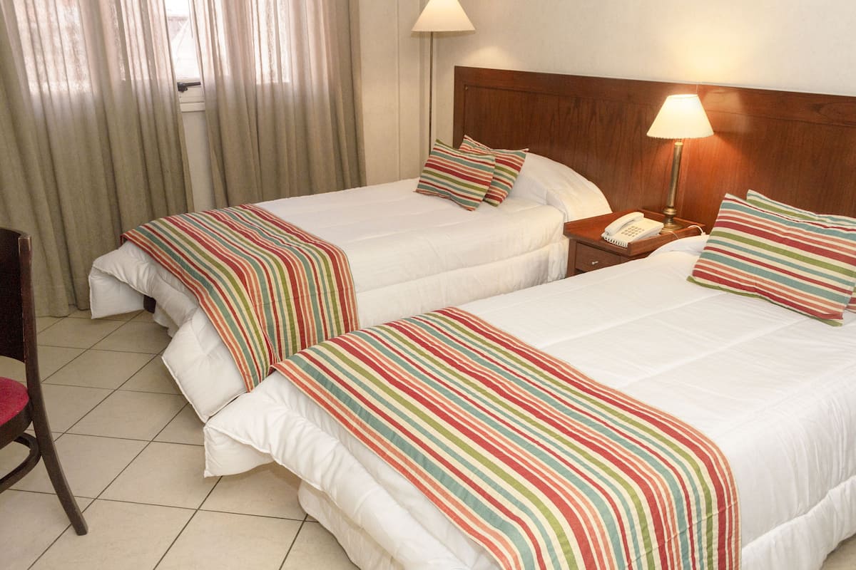 Two single beds with striped bedding, a wooden headboard, a nightstand with a lamp, and a chair.