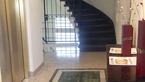 Interior modern amb una escala, un senyal que diu "SALIDA DE EMERGENCIA" i una taula de recepció amb un vas de branques.