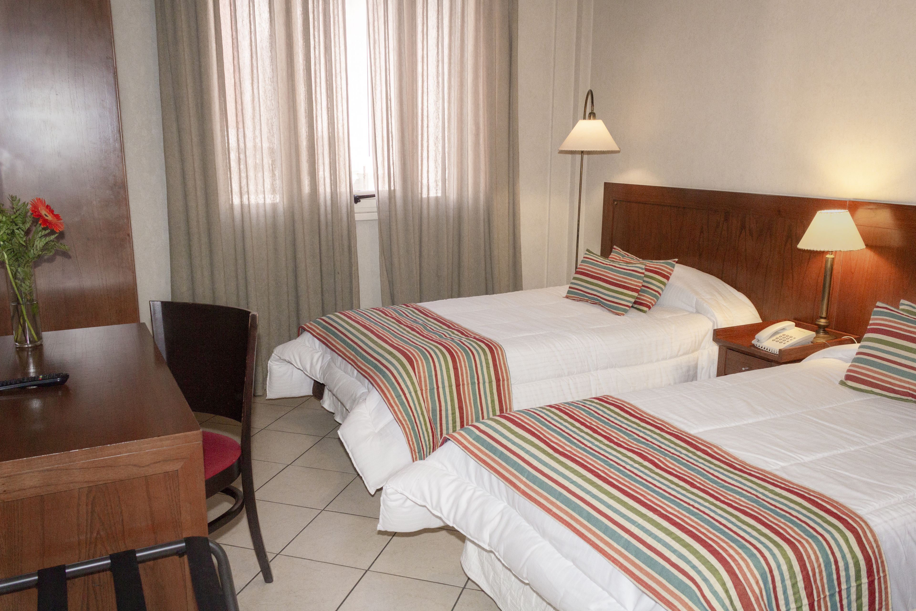 A hotel room with two beds, a desk, a chair, and a window with curtains.