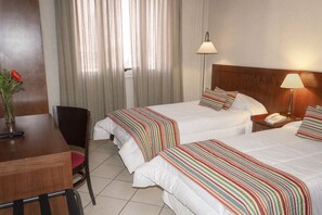 Una habitació d'hotel amb dos llits, un escriptori, una cadira i una finestra amb cortines.