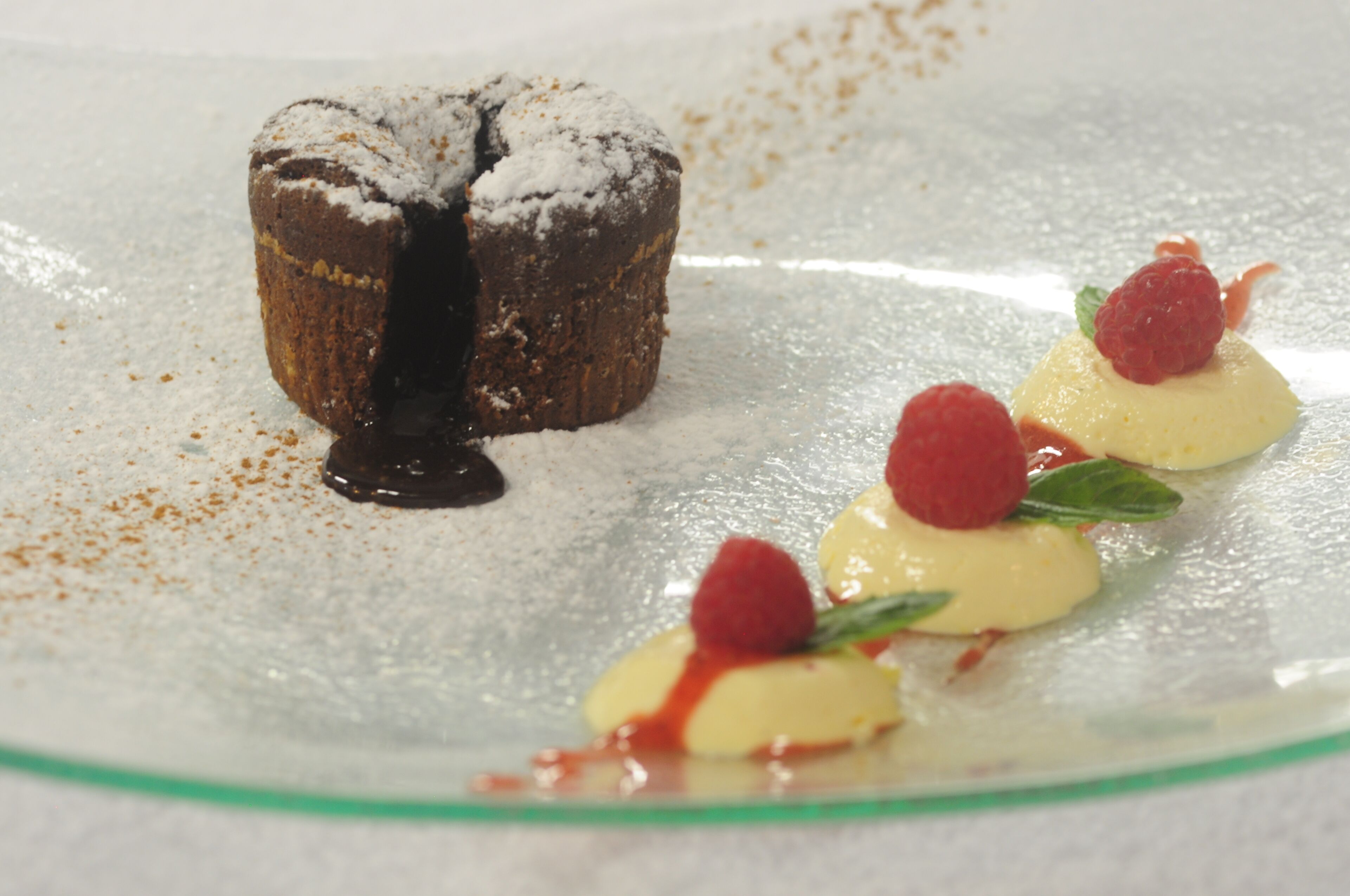 Ein Dessertteller mit einem Schokoladenküchlein und Sahne mit Himbeeren.