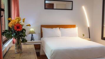 A hotel room with a bed, a nightstand, a lamp, a vase with flowers, and a mirror on the wall.