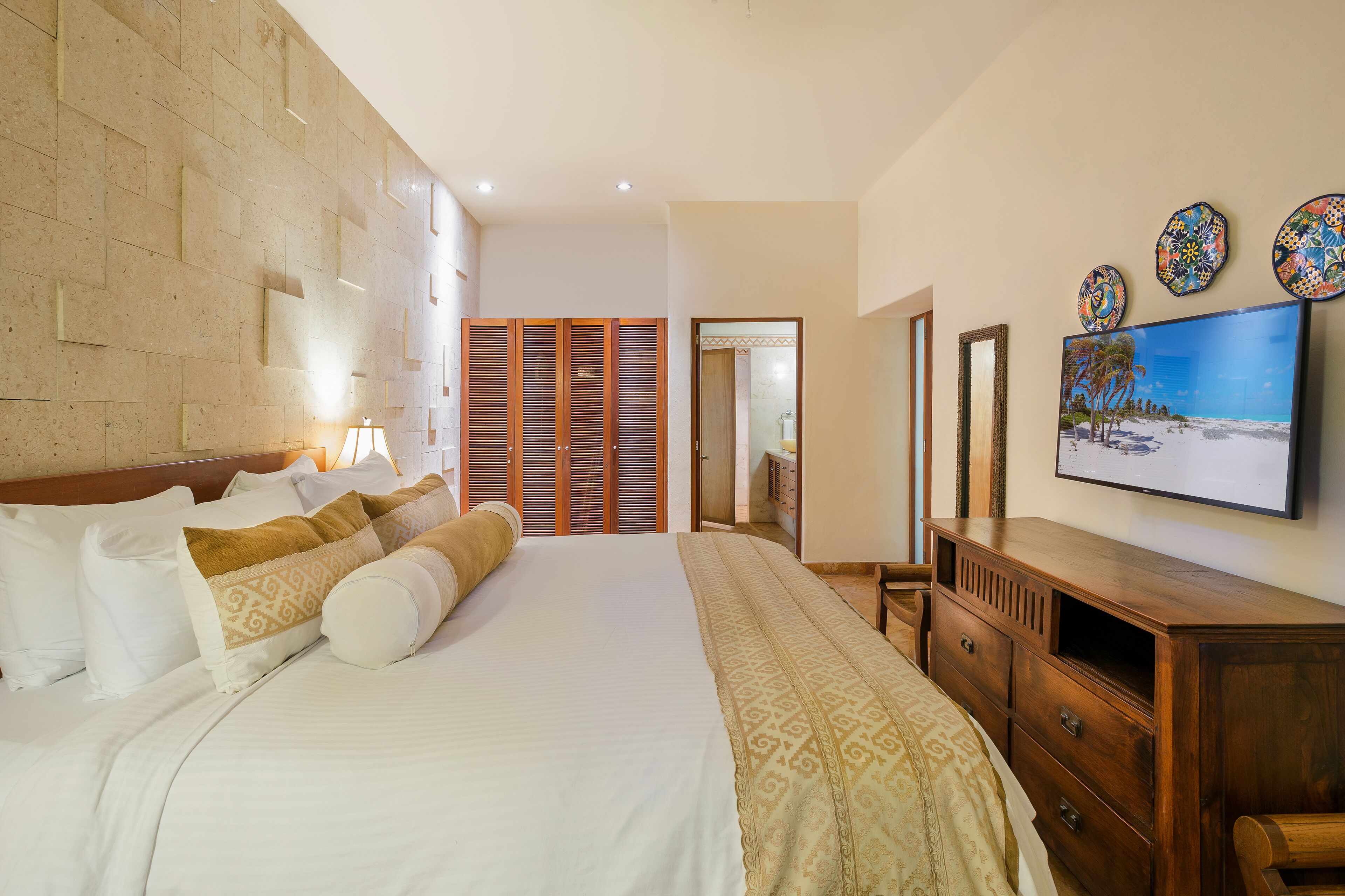 Habitación de hotel con una cama grande, un armario de madera y un televisor en la pared.