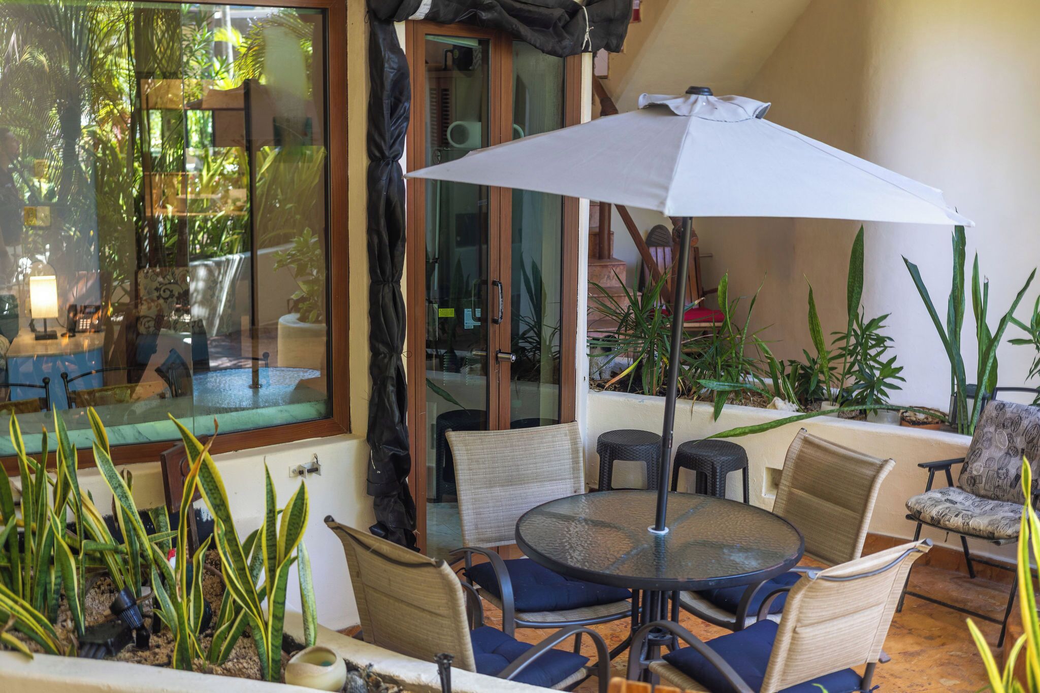 Un espace extérieur aménagé avec une table ronde et des chaises, un grand parasol et diverses plantes.