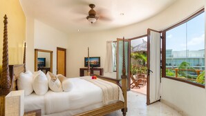 A spacious bedroom with a large bed, a ceiling fan, a TV, and a balcony with a view of palm trees and a building. - Porto Playa Condo Hotel & Beachclub (Playa del Carmen)