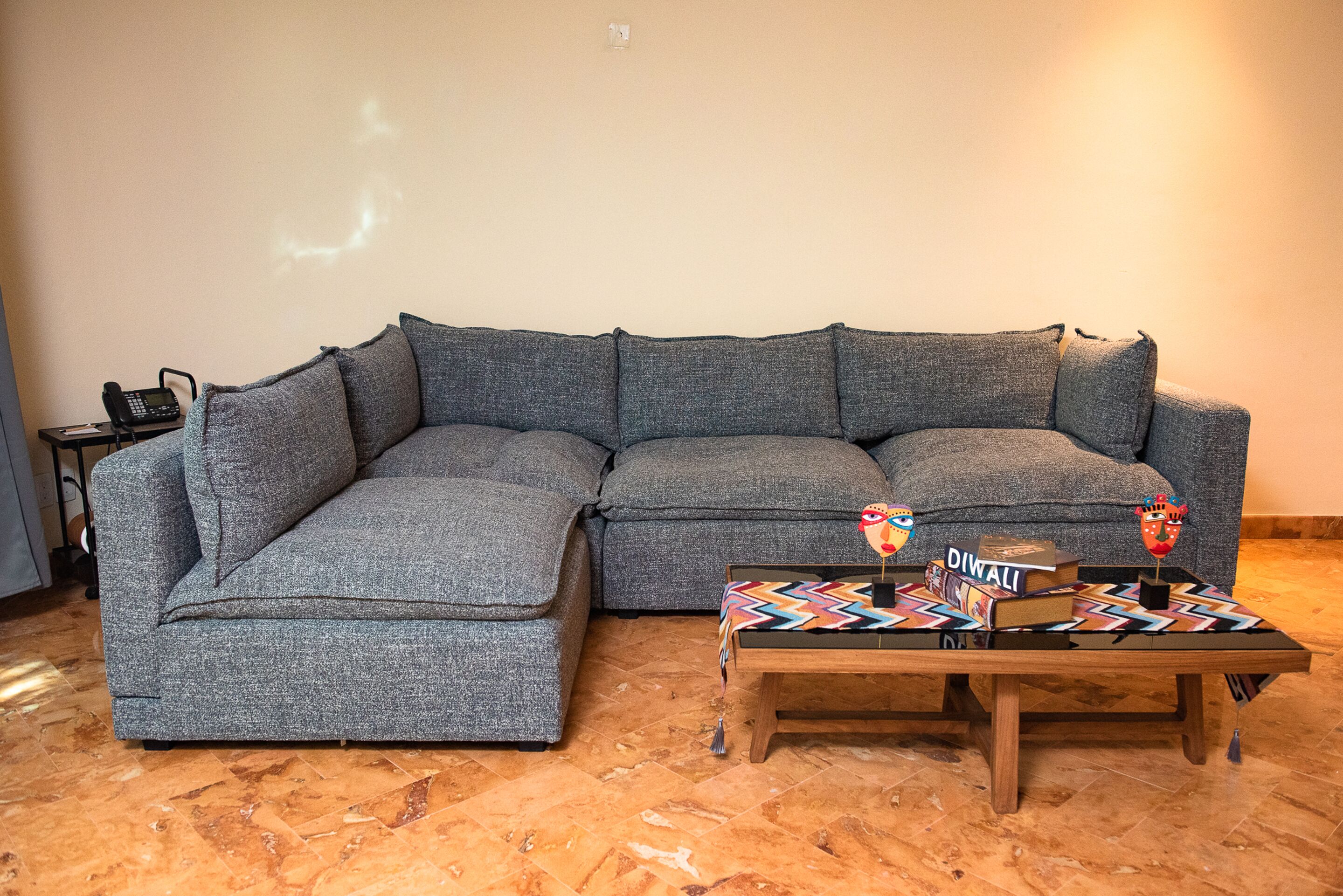 A grey sectional sofa with a wooden coffee table in front, a telephone on the left, and a wall with a light switch.