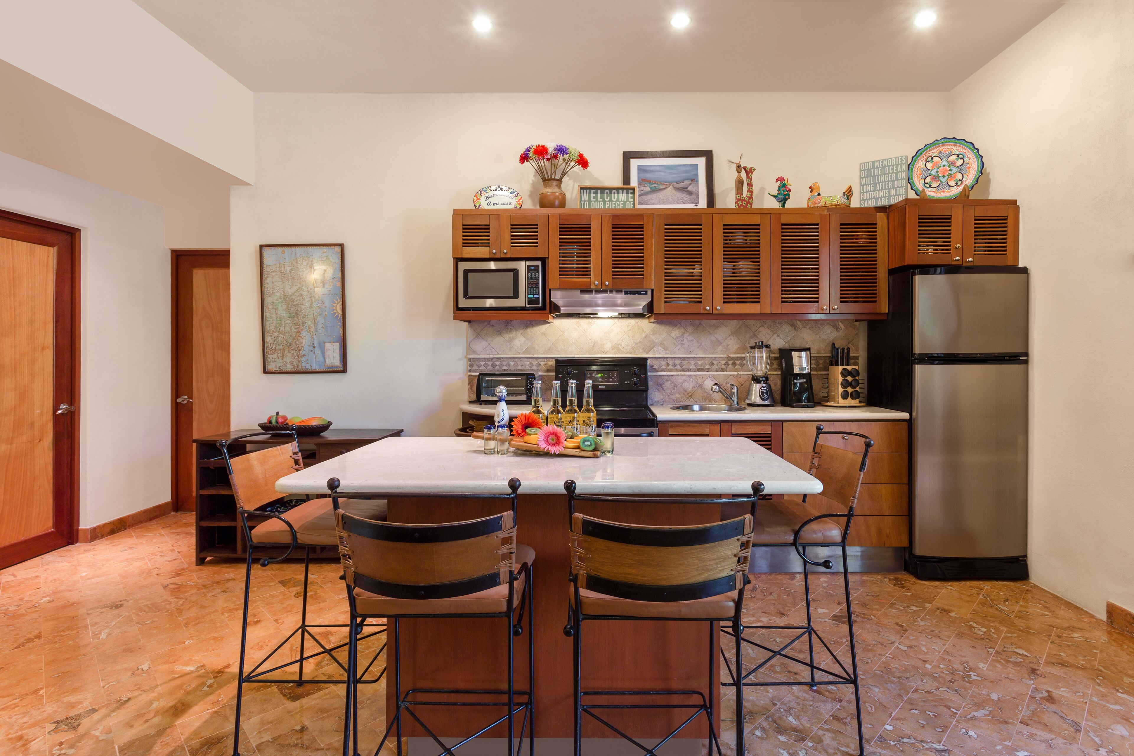 Una cocina con una isla central, taburetes de bar, armarios de madera, un refrigerador de acero inoxidable y un microondas.