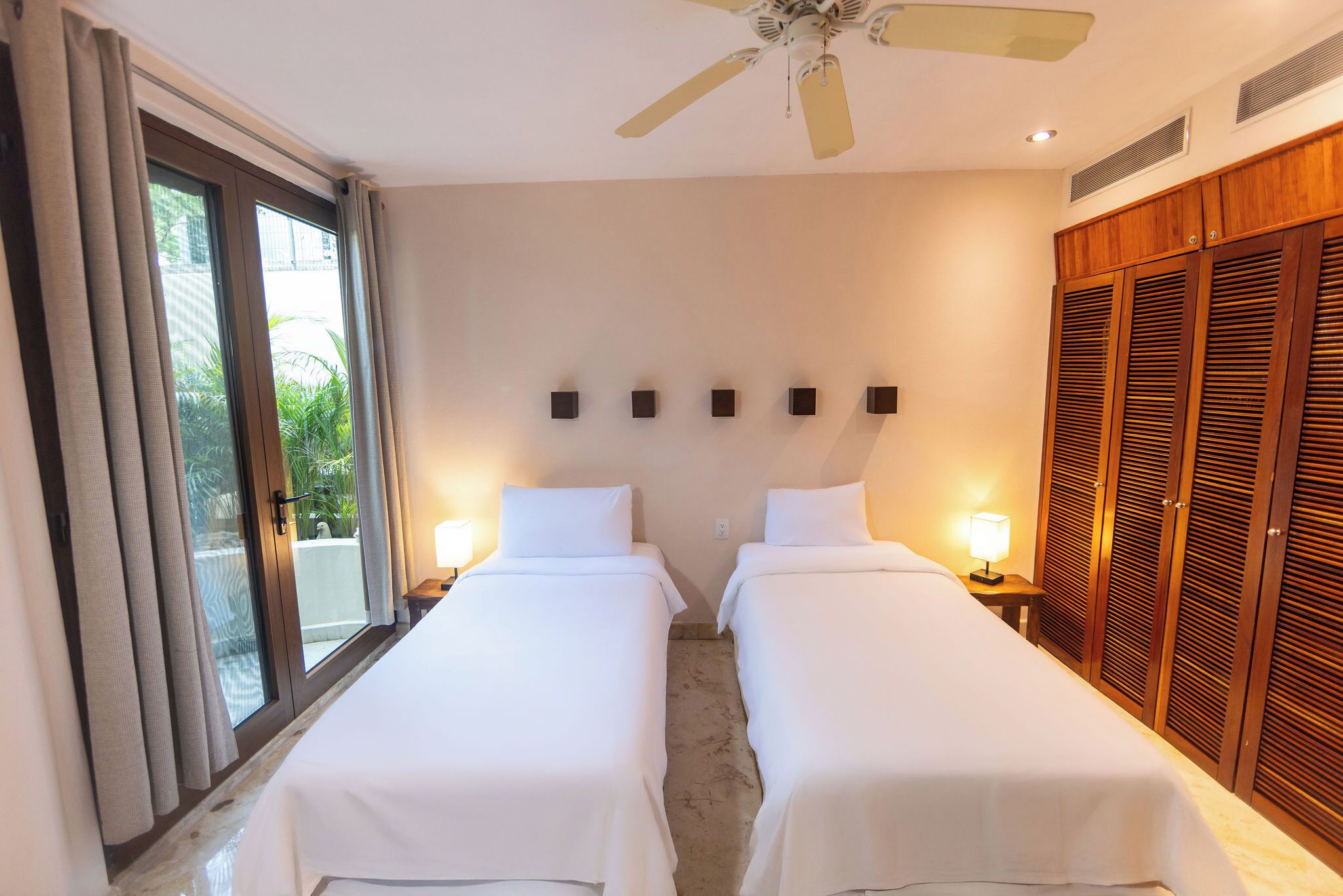 Een hotelkamer met twee bedden, een schuifdeur, een plafondventilator en een houten kledingkast.
