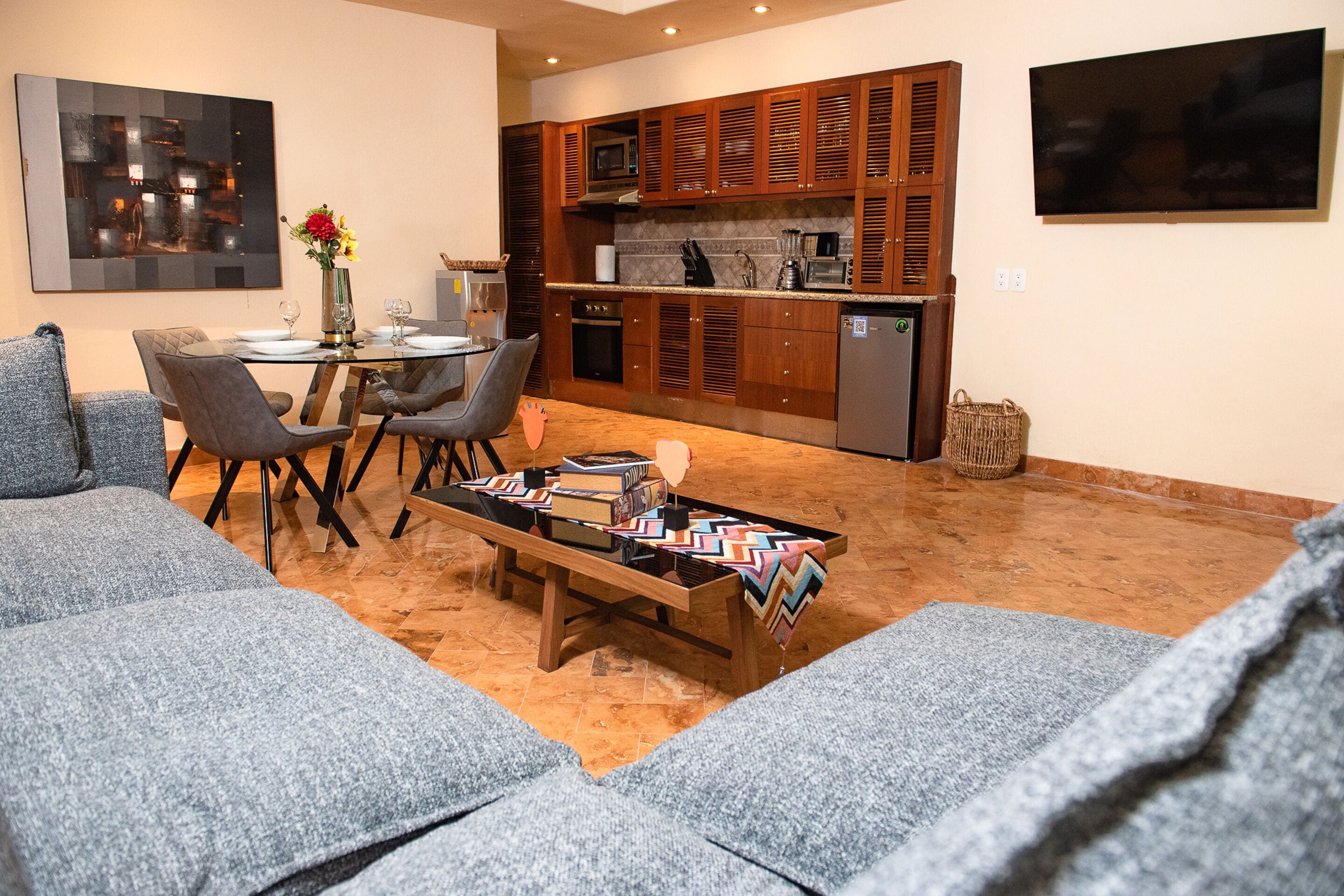A modern living room with grey sofas, a coffee table, and a dining area with chairs and a table.