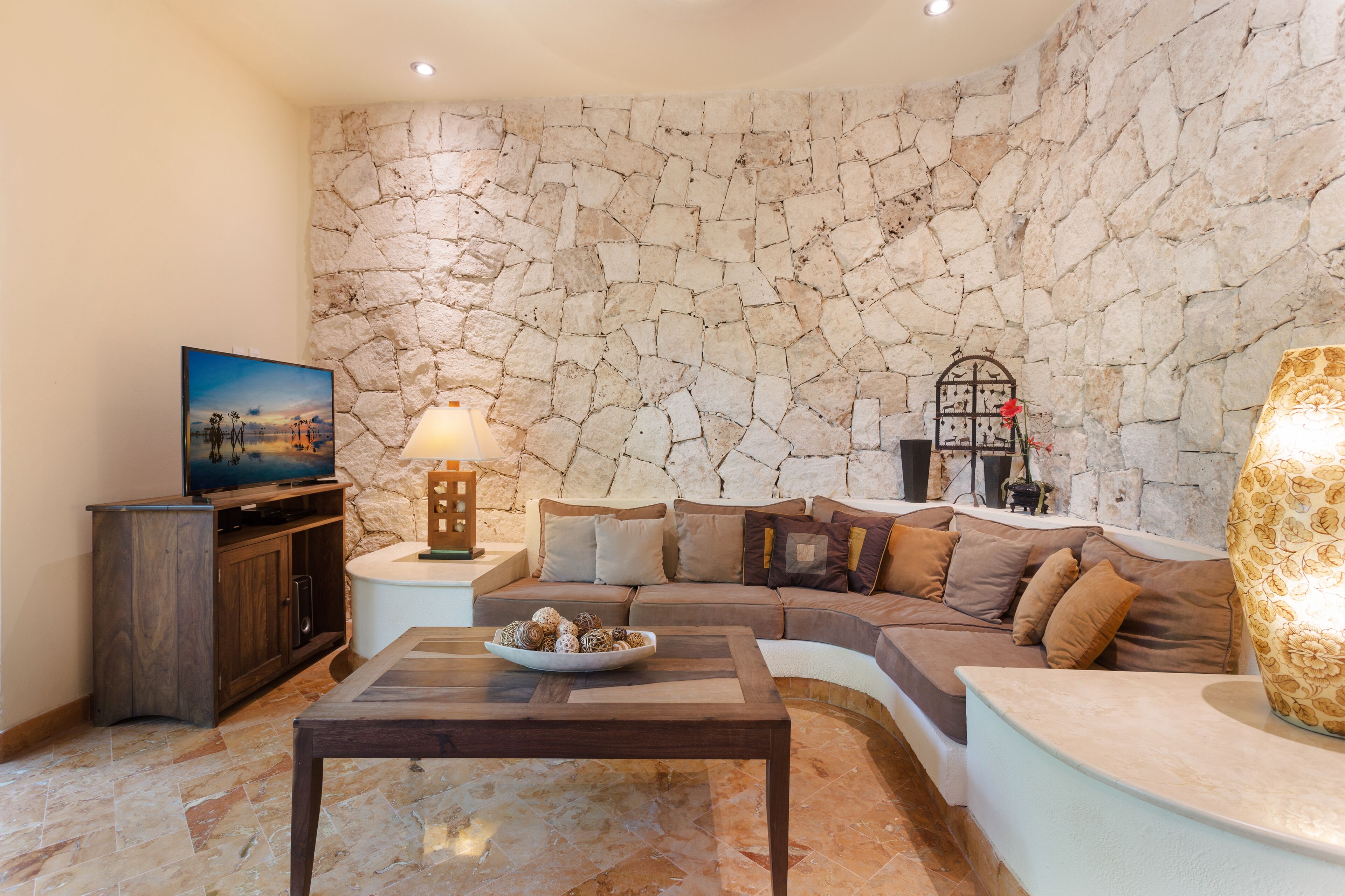 Ein Wohnzimmer mit Steinsandsteinwand, einer Couch, einem Couchtisch, einem Fernseher und einer Lampe.