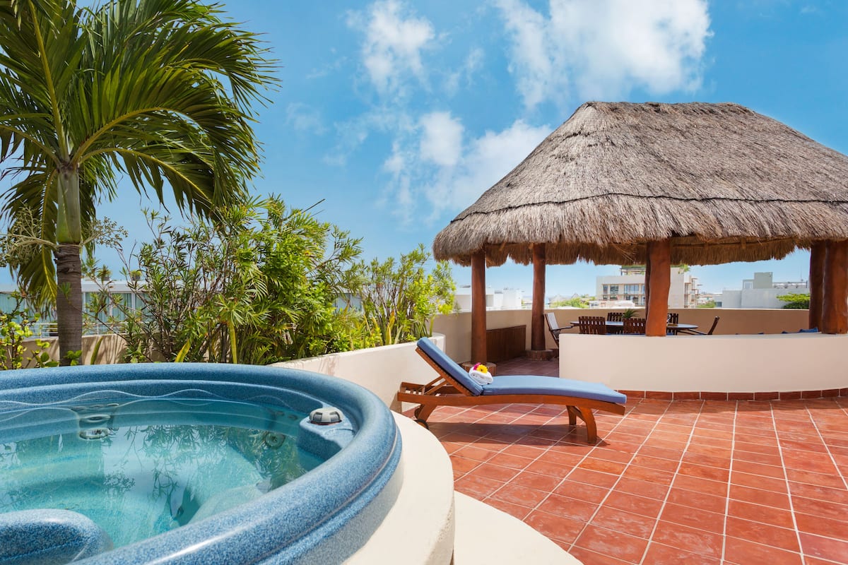 Un bain à remous avec des chaises longues, un gazebo à toit de chaume et un palmier.