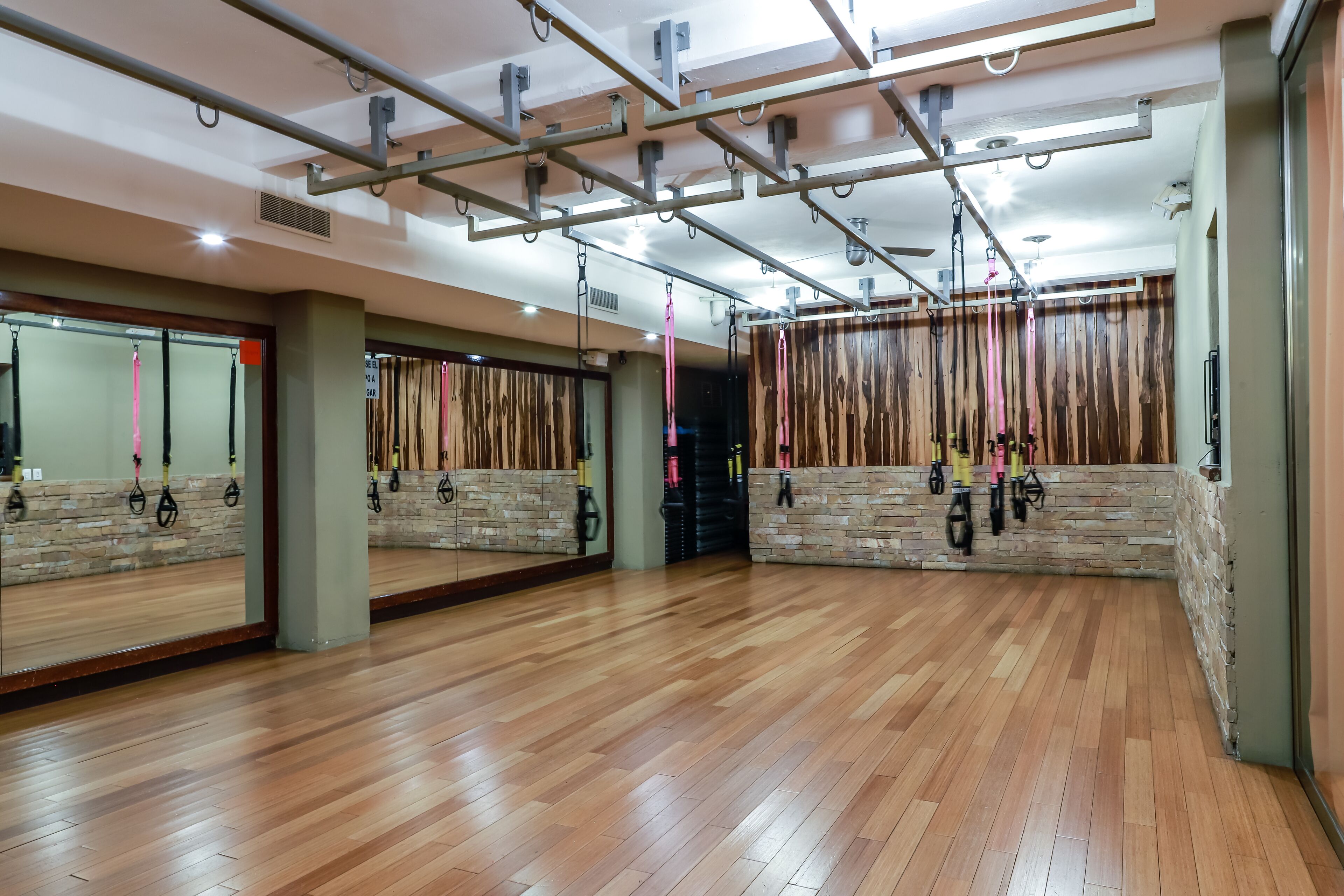A spacious room with wooden flooring, a large mirror, and exercise equipment like resistance bands and ropes.
