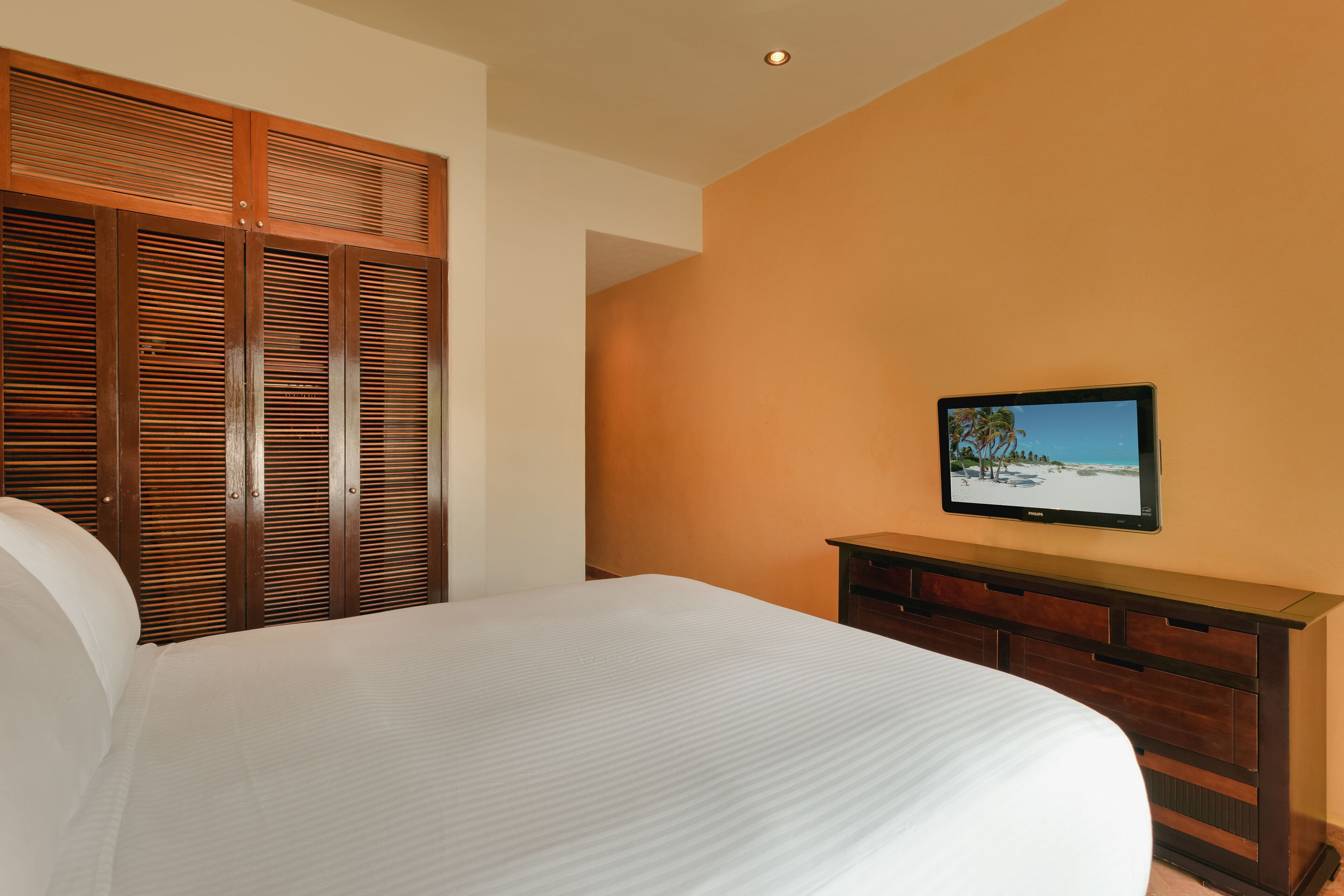 Une chambre à coucher avec un lit, une armoire en bois et un téléviseur posé sur une commode.