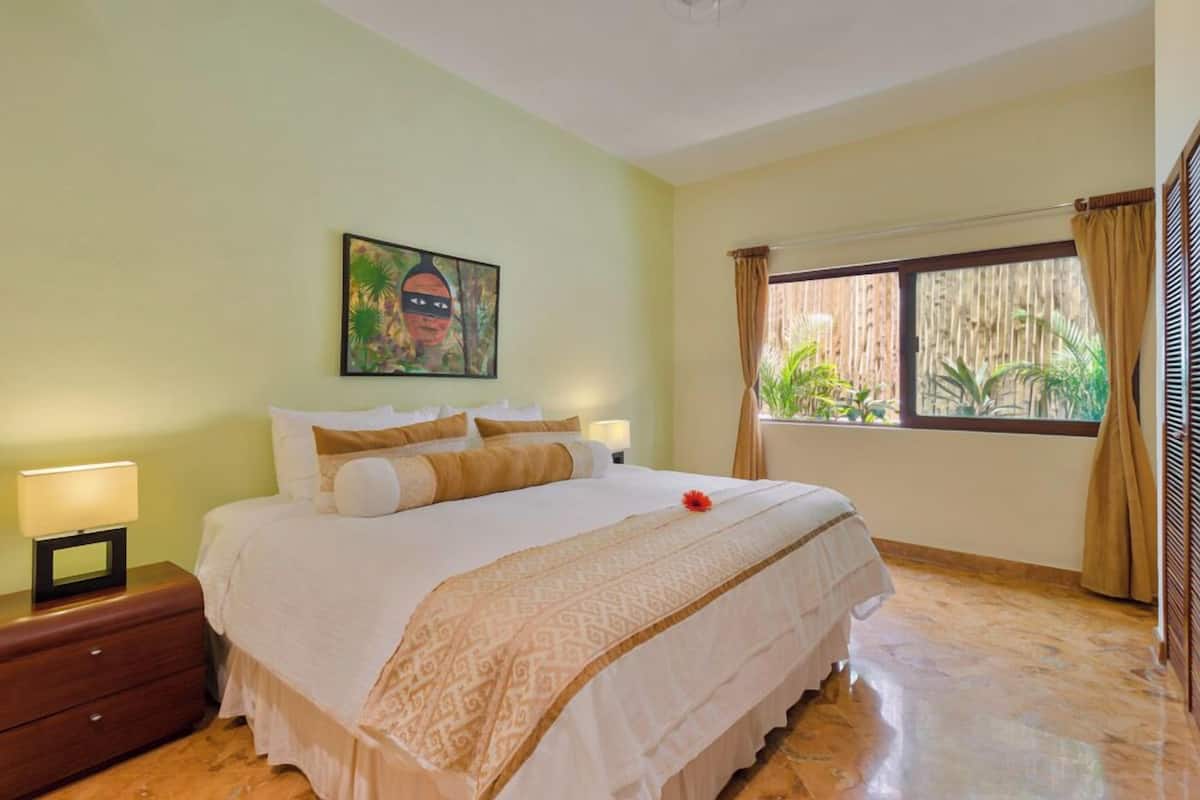 Une chambre d’hôtel avec un lit, des tables de chevet, une fenêtre avec des rideaux et un tableau au mur.