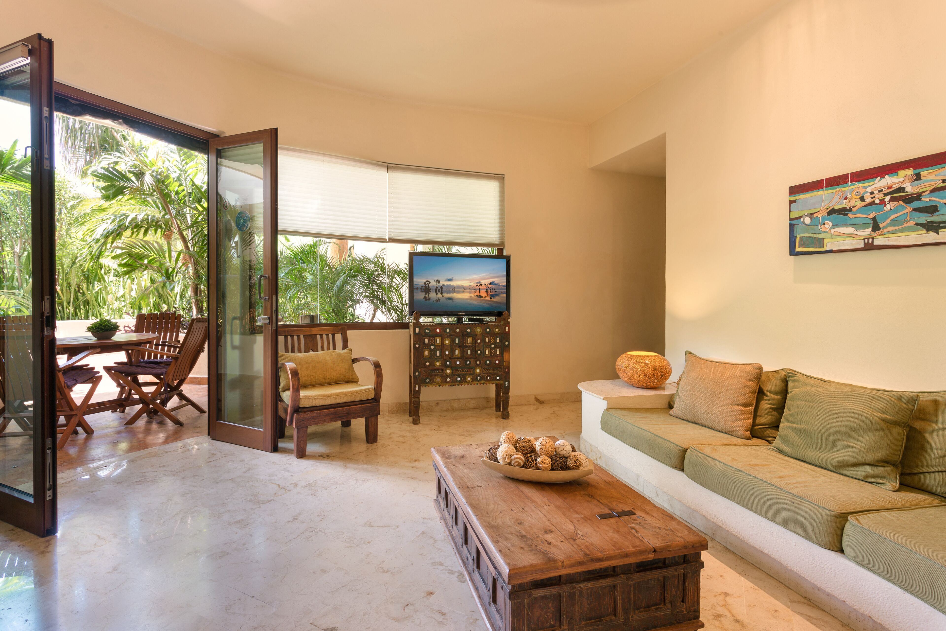 A living room with a sofa, a coffee table, and a TV. There is a dining area with chairs and a table.