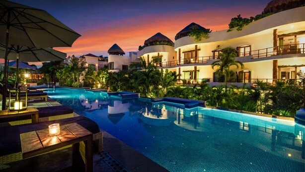 A resort with a large swimming pool, lounge areas, and multiple buildings with thatched roofs. - Porto Playa Condo Hotel & Beachclub (Playa del Carmen)