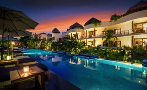 Un resort con una amplia piscina, zonas de descanso y varias edificaciones con techos de paja.