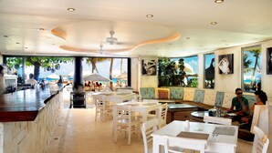 A restaurant with white furniture, a bar, and large windows overlooking the beach. - Porto Playa Condo Hotel & Beachclub (Playa del Carmen)