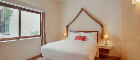 Una cama bien hecha con cabecera de madera, dos lámparas de noche y una ventana con cortinas.