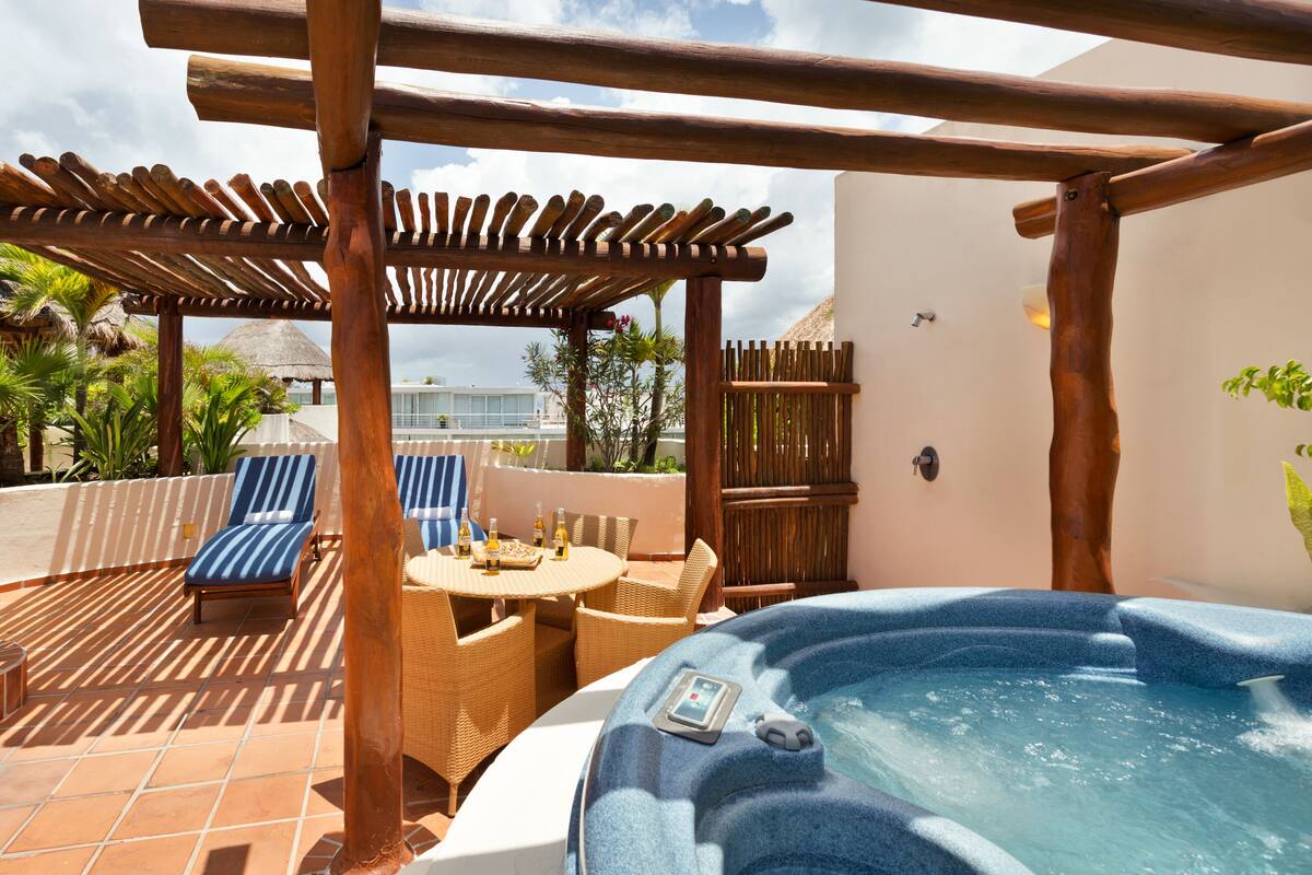 Un bain à remous doté d’un panneau de commande, un espace de détente couvert avec des chaises longues et une terrasse carrelée.