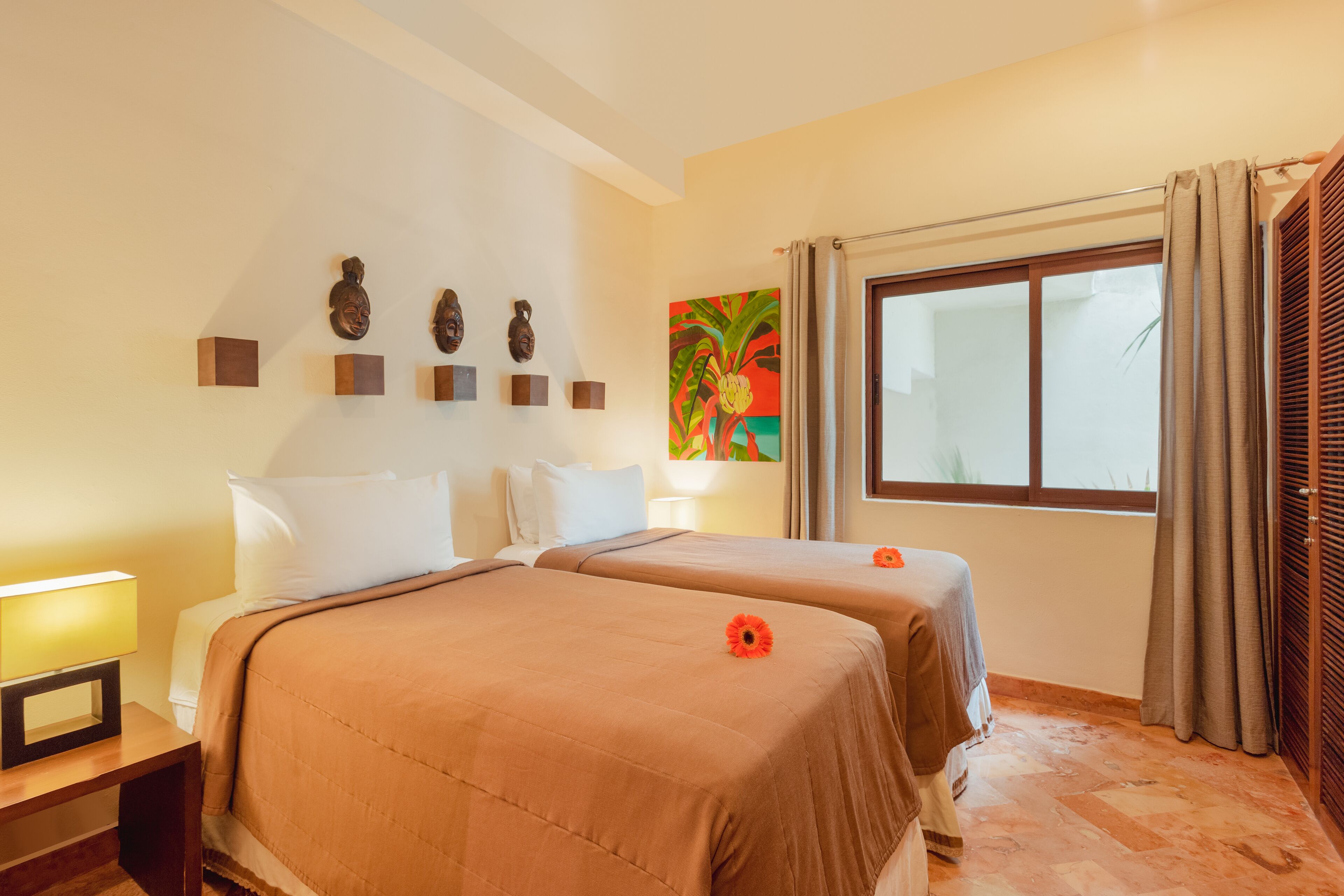 Habitación de hotel con dos camas, una ventana con cortinas, un cuadro en la pared y una mesita de noche con lámpara.