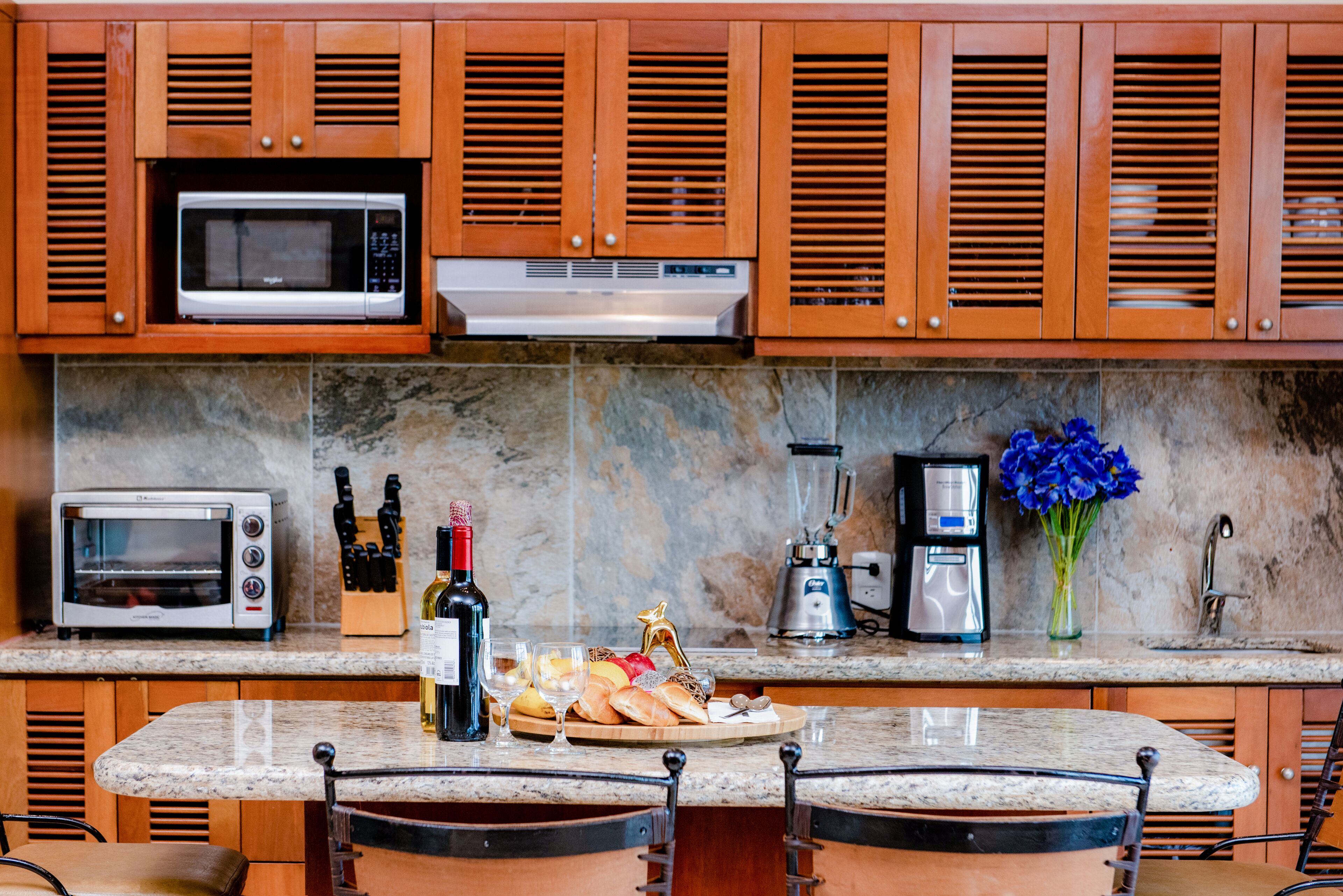 Una cocina con armarios de madera, microondas, tostadora, cafetera y una botella de vino.