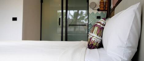 A hotel room with a bed, a glass door leading to a balcony, and a view of palm trees.