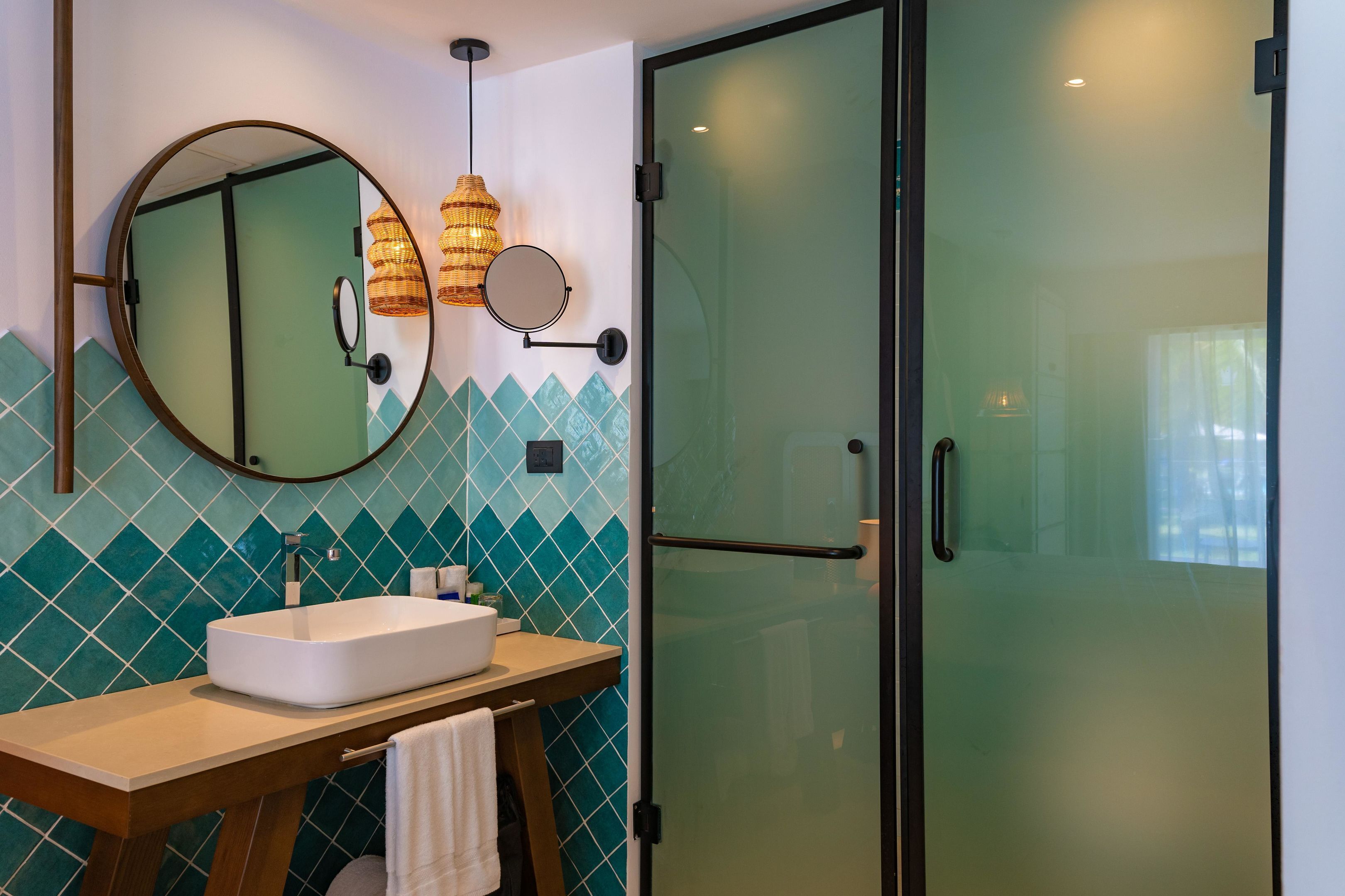 Une salle de bain avec un lavabo blanc, un miroir rond et une porte de douche en verre.