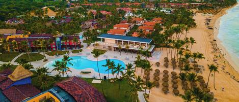 A resort with a central pool, beach, and palm trees.