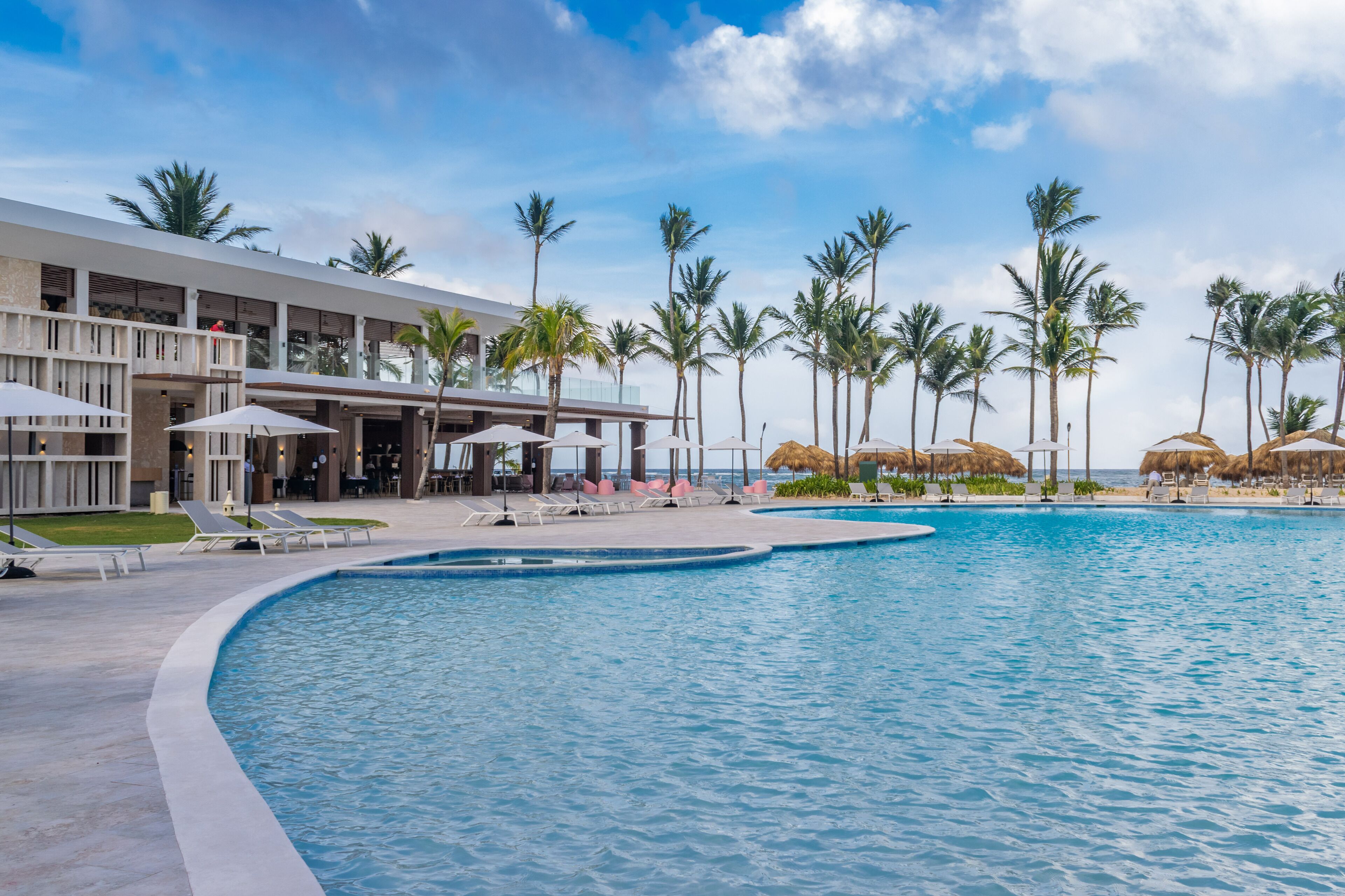 A resort pool area with lounge chairs, umbrellas, and palm trees.