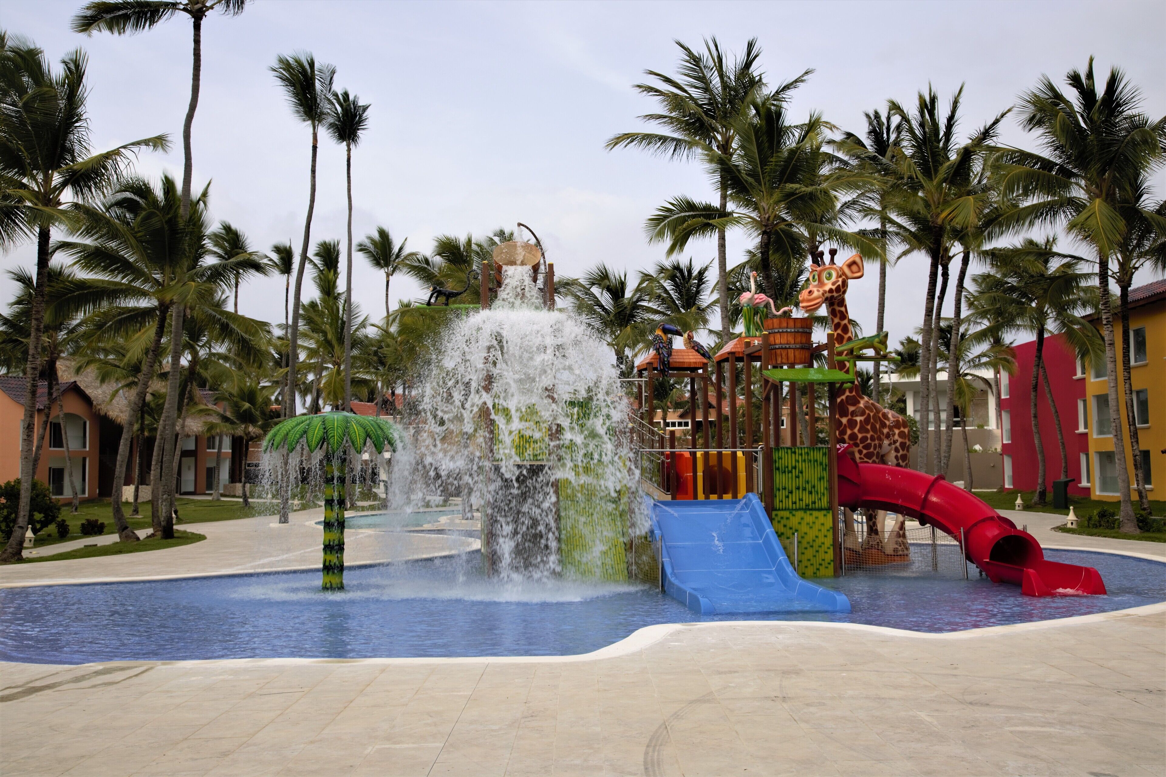 Un parque acuático con una fuente central, toboganes y una estatua de jirafa.