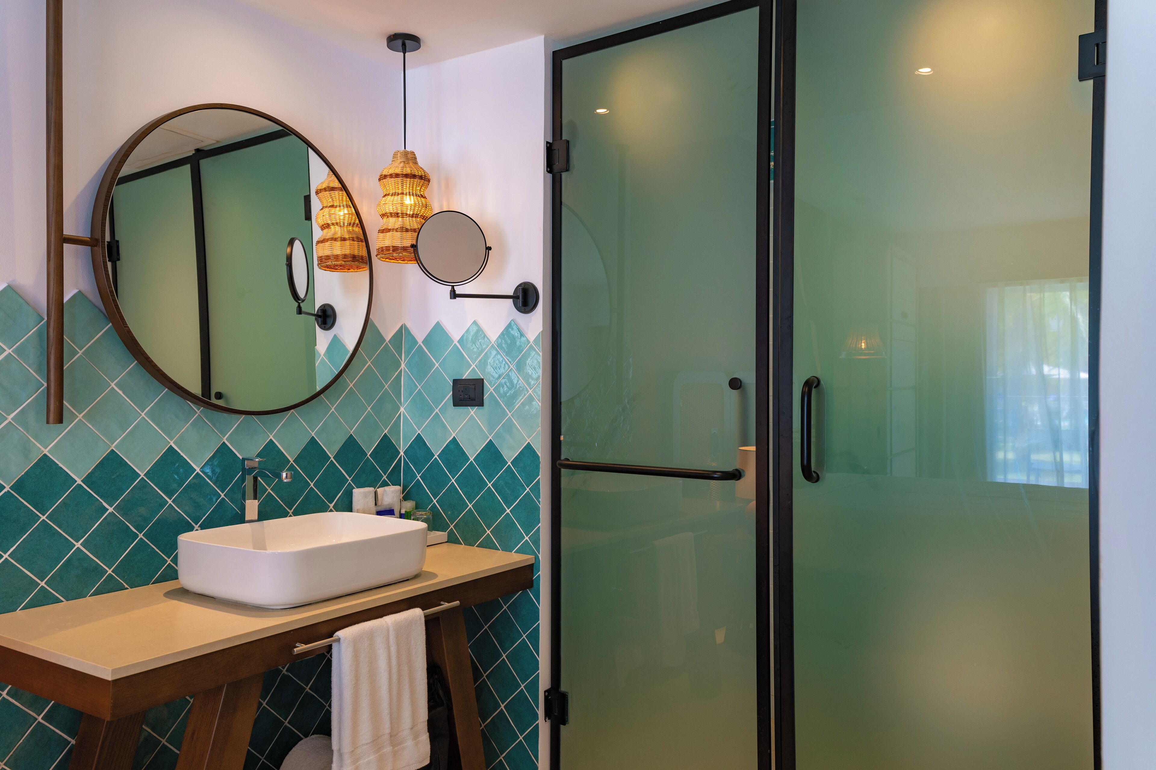A bathroom with a white sink, a round mirror, and a glass shower enclosure.