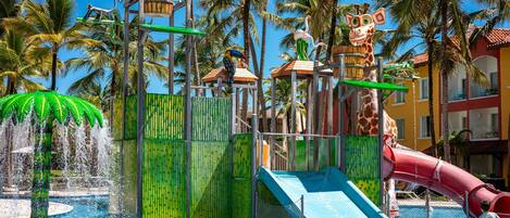 A water park with slides and a pool, surrounded by palm trees and a building with a red roof.