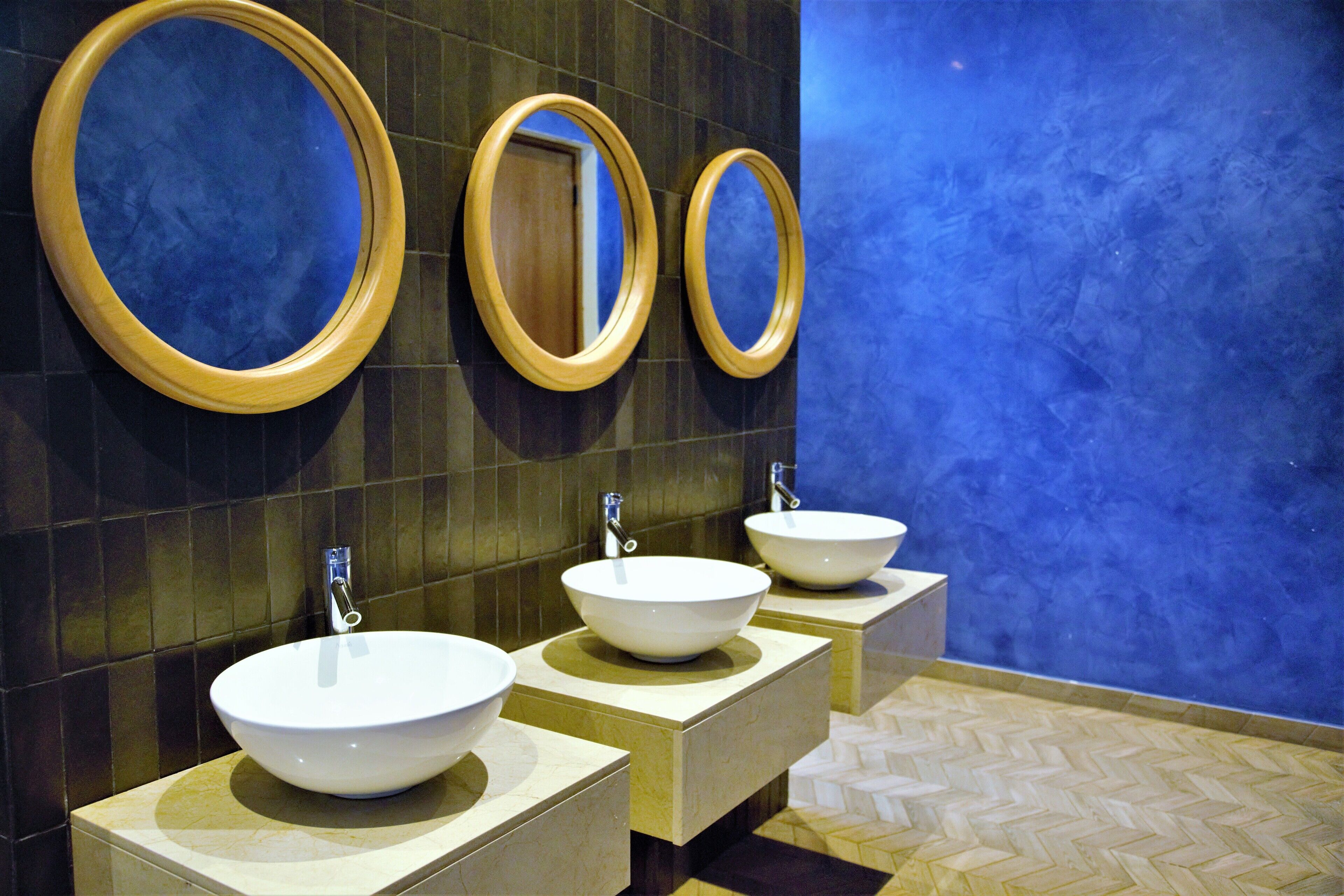 Une salle de bain avec trois lavabos, chacun surmonté d’un miroir encadré en bois.