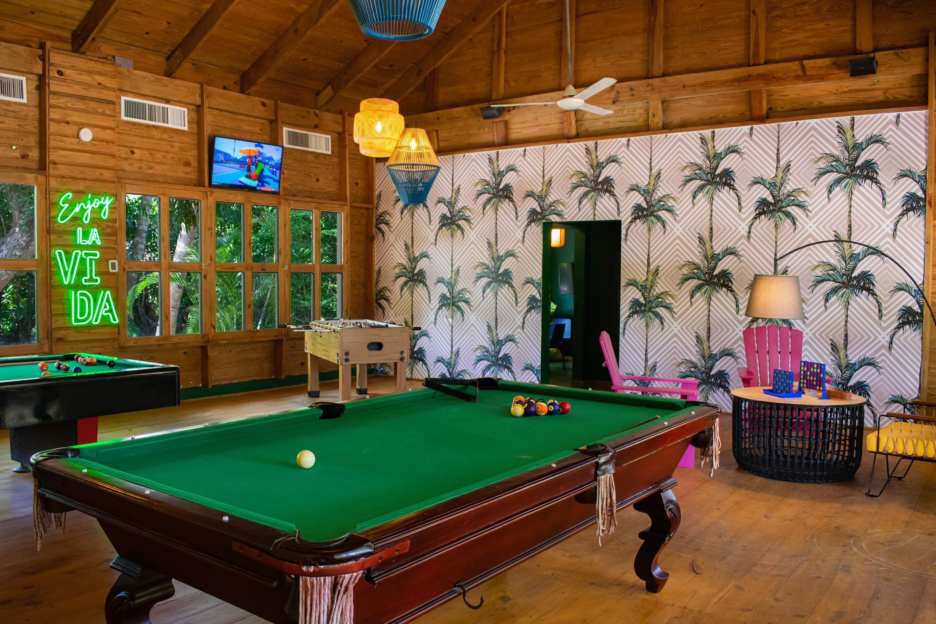A pool table in a wooden room with a neon sign, a television, and a patterned wall.