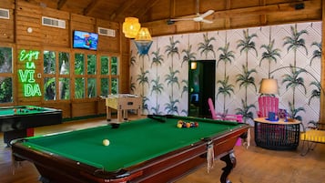 A pool table in a wooden room with a neon sign, a television, and a patterned wall.