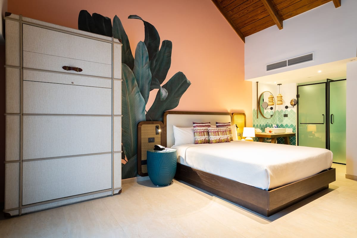 Un dormitorio con cama, armario, una planta grande y baño con ducha e inodoro.