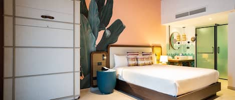 A bedroom with a large bed, a wardrobe, a round table, and a wall with a large plant.