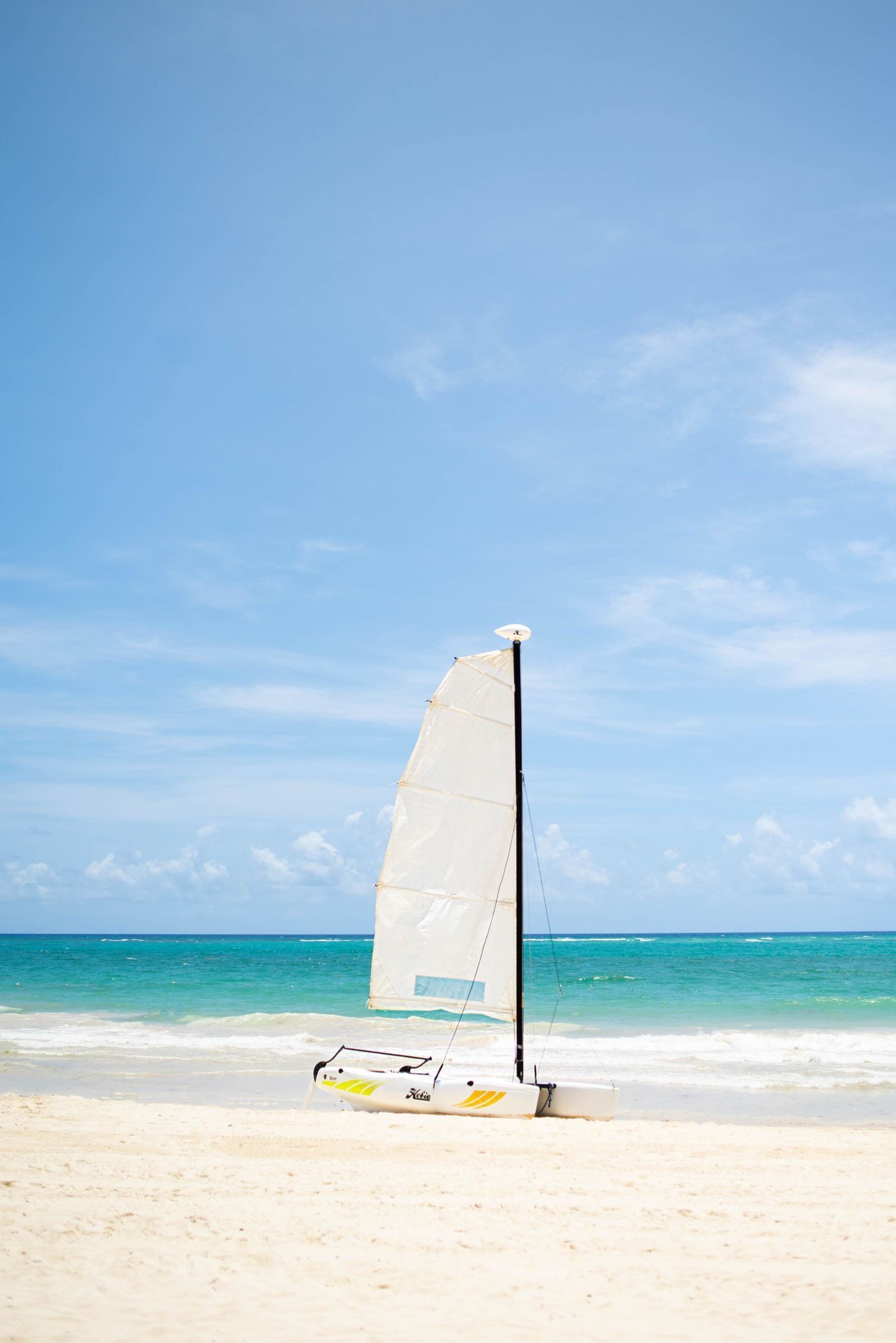 A sailboat on a sandy beach with clear blue water and a clear sky.