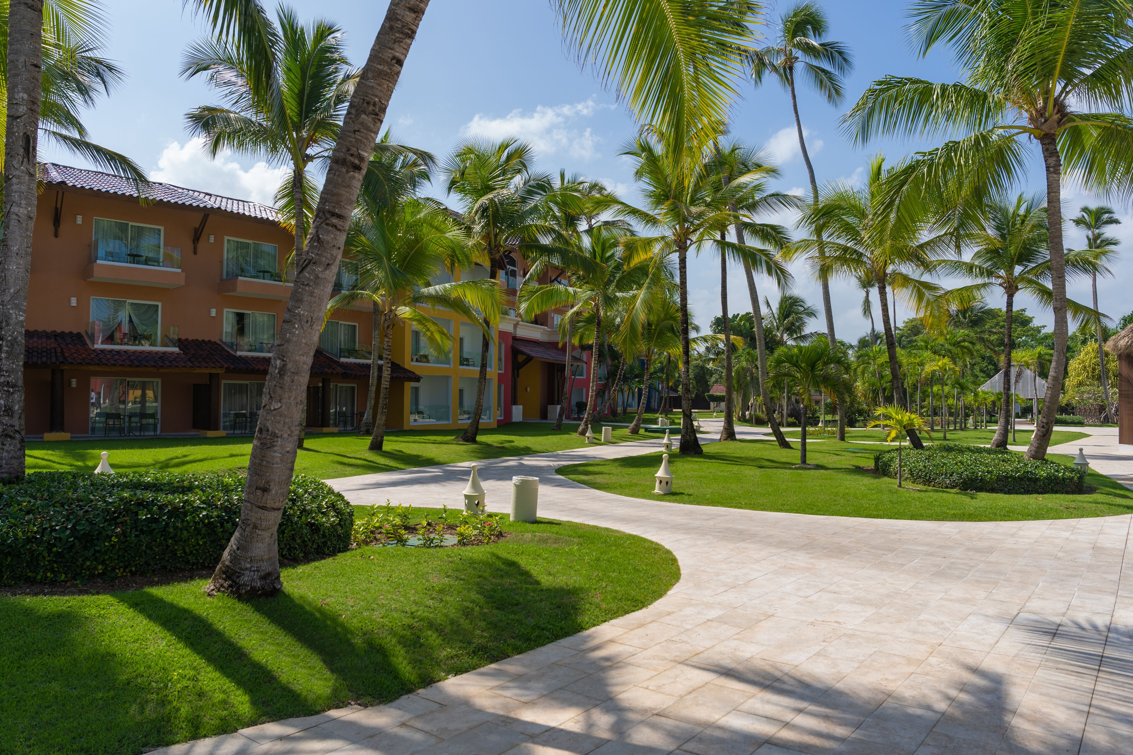 A resort with a paved walkway, palm trees, and a building with multiple balconies.