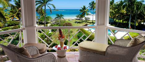 A balcony with wicker furniture, a table with a vase, and a view of a beach and ocean.