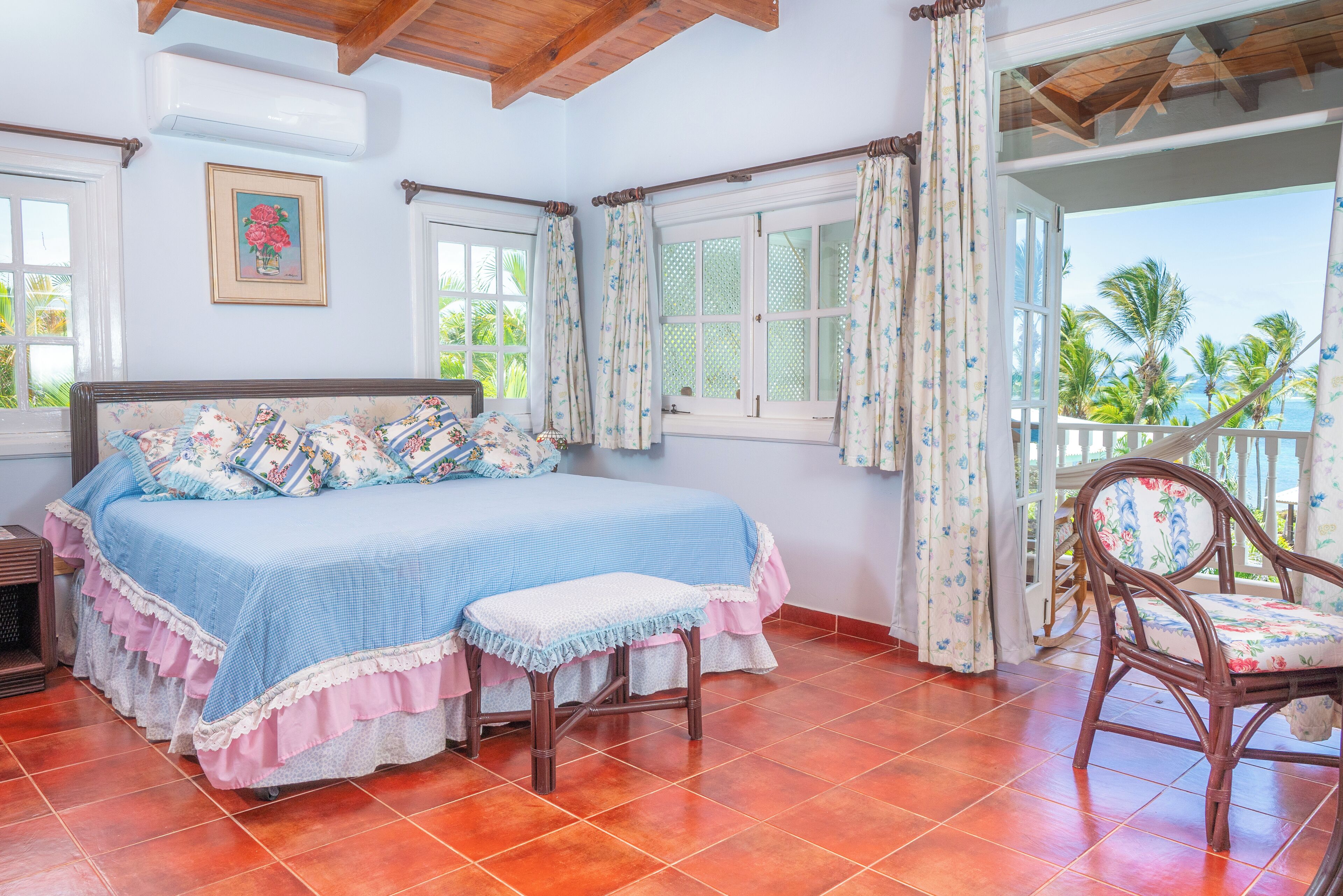 A bedroom with a bed, a chair, and a view of palm trees.