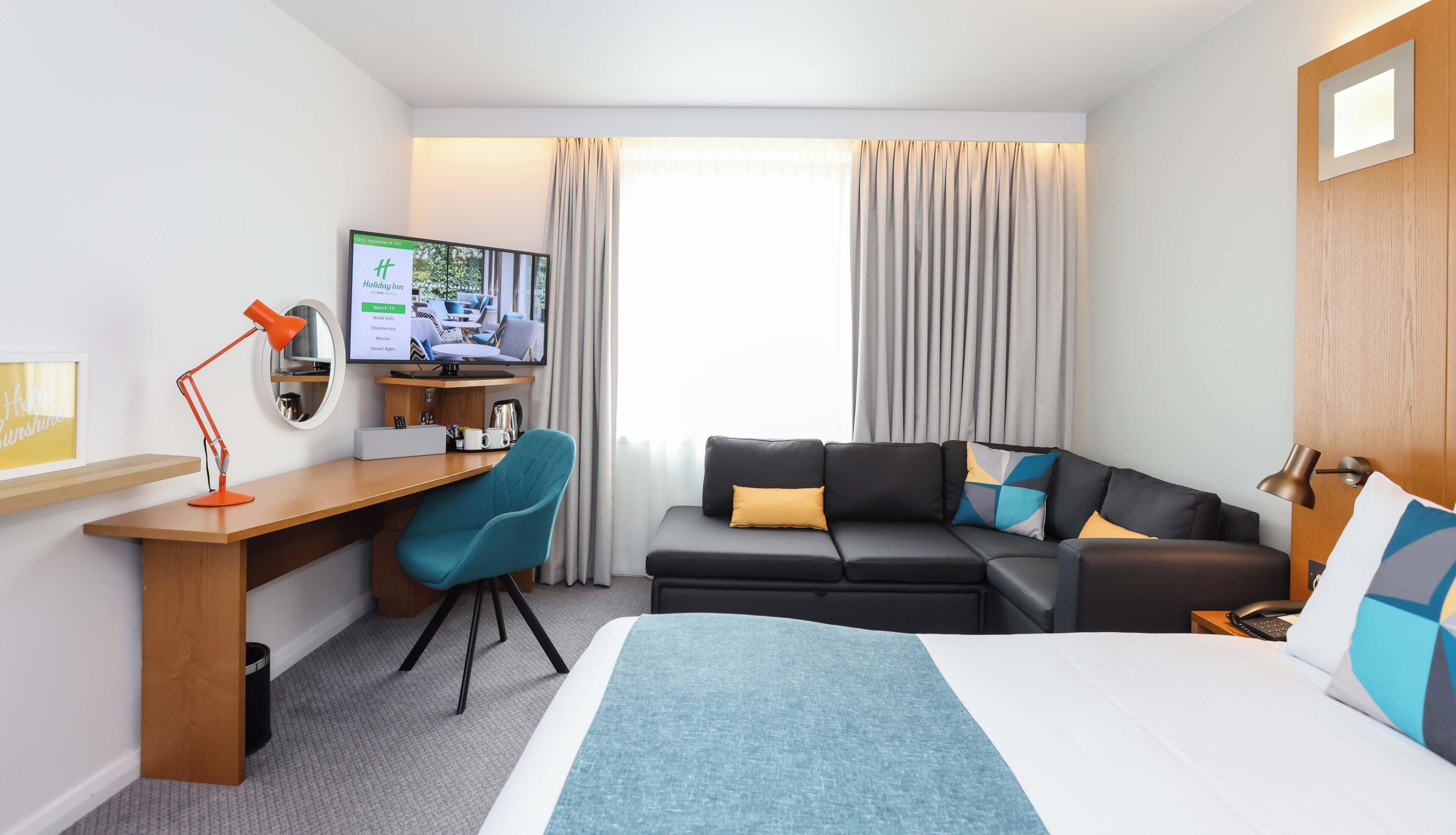 Una habitación de hotel con una cama, un escritorio con una computadora, un televisor y un sofá.