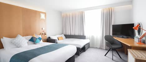 A hotel room with a bed, a desk, a chair, a television, and a window with curtains.