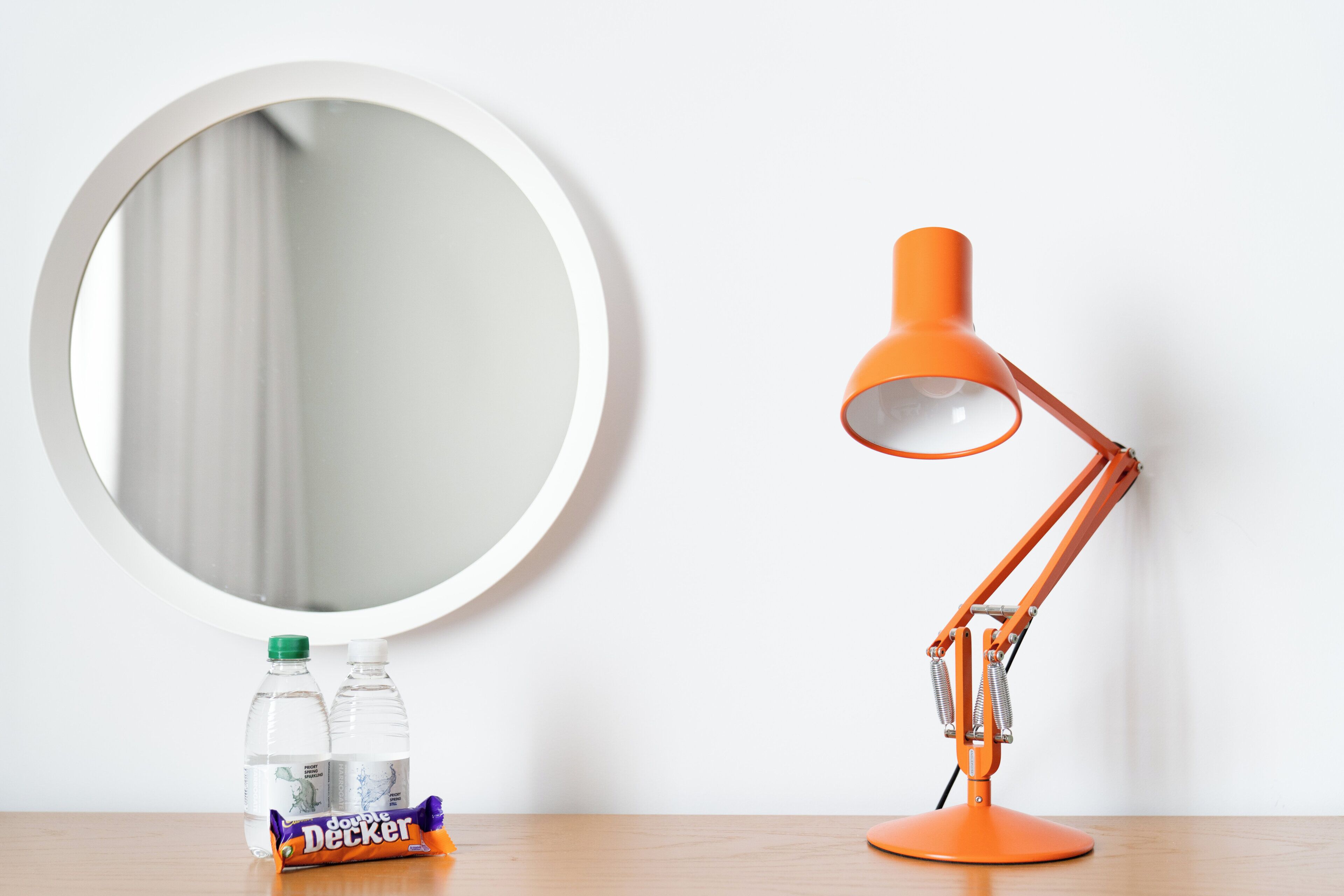 A round mirror, an orange desk lamp, and two bottles of water on a wooden surface.