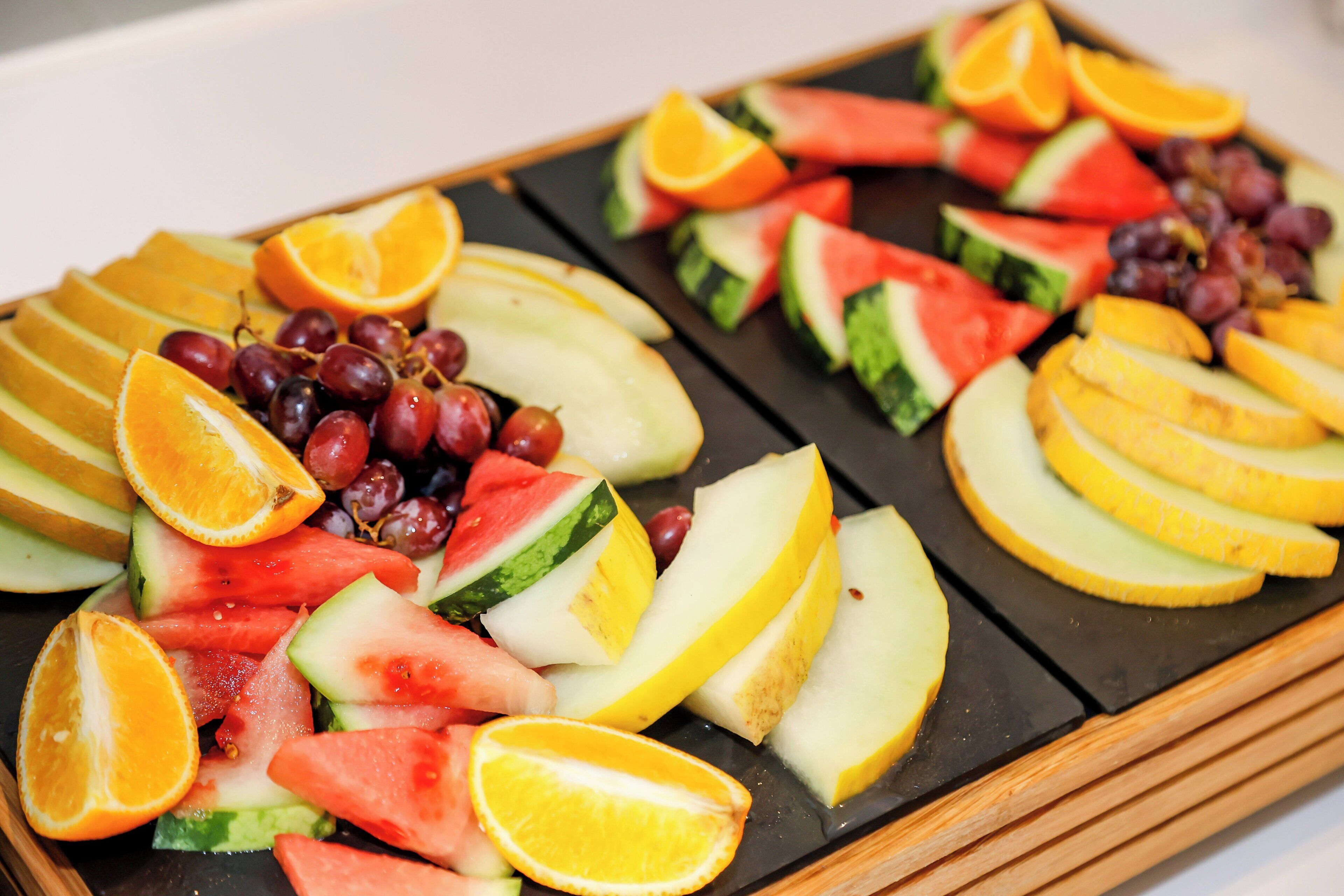 A tray of assorted fruits including watermelon, oranges, and grapes.