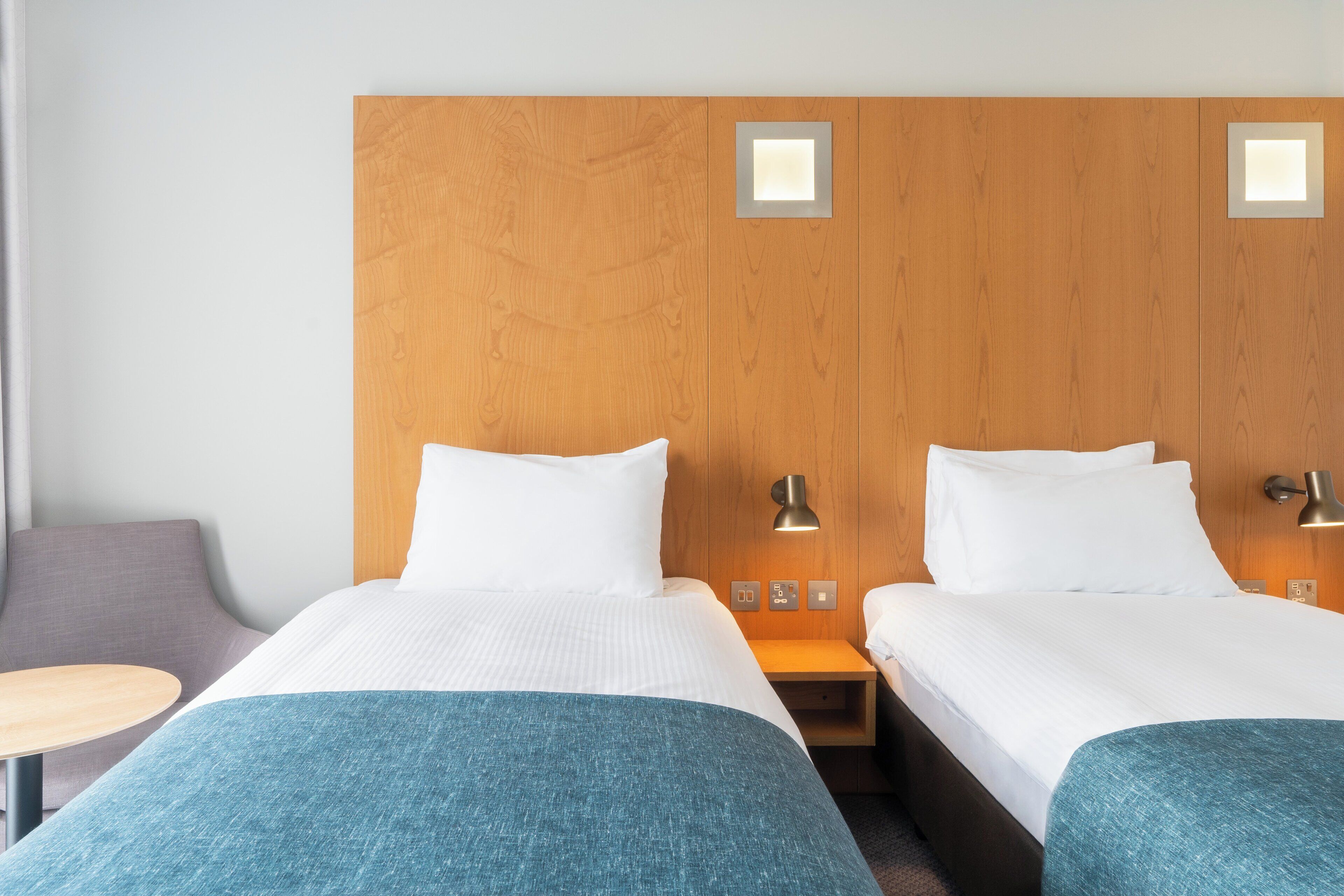 Een hotelkamer met twee bedden, een nachtkastje, een lamp en een klein tafeltje.